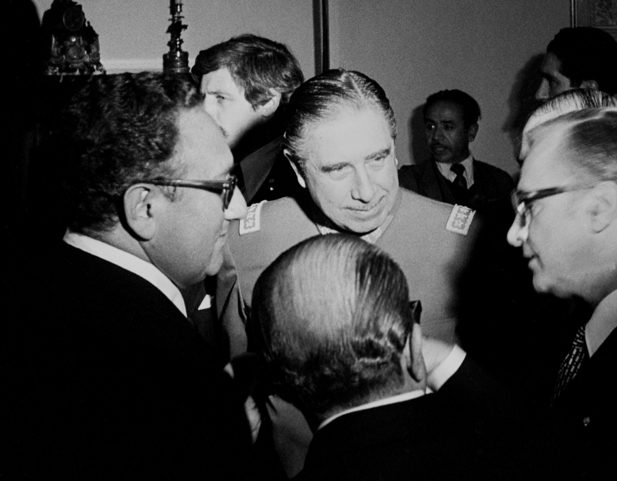 Henry Kissinger and Augusto Pinochet stand in a small circle of men.
