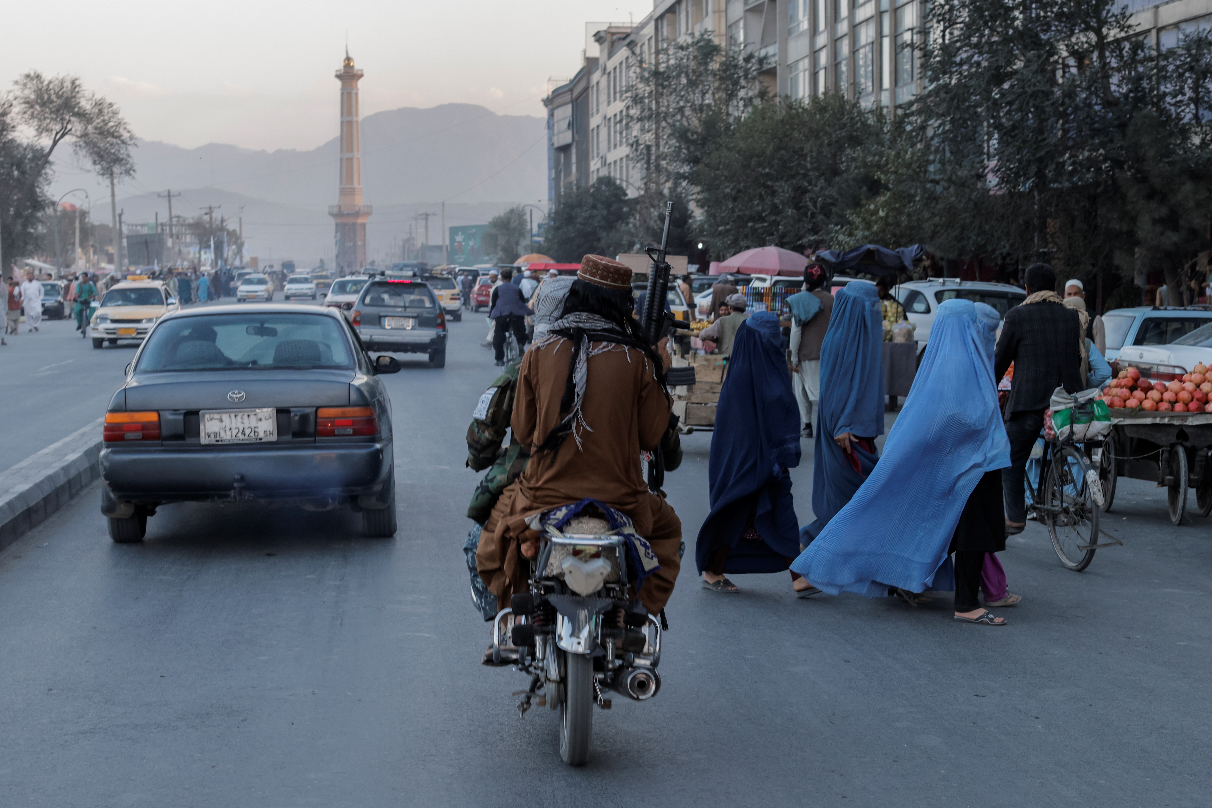 A group of women wearing burqas crosses the street as members of the Taliban drive past in Kabul, Afghanistan [Jorge Silva/Reuters]