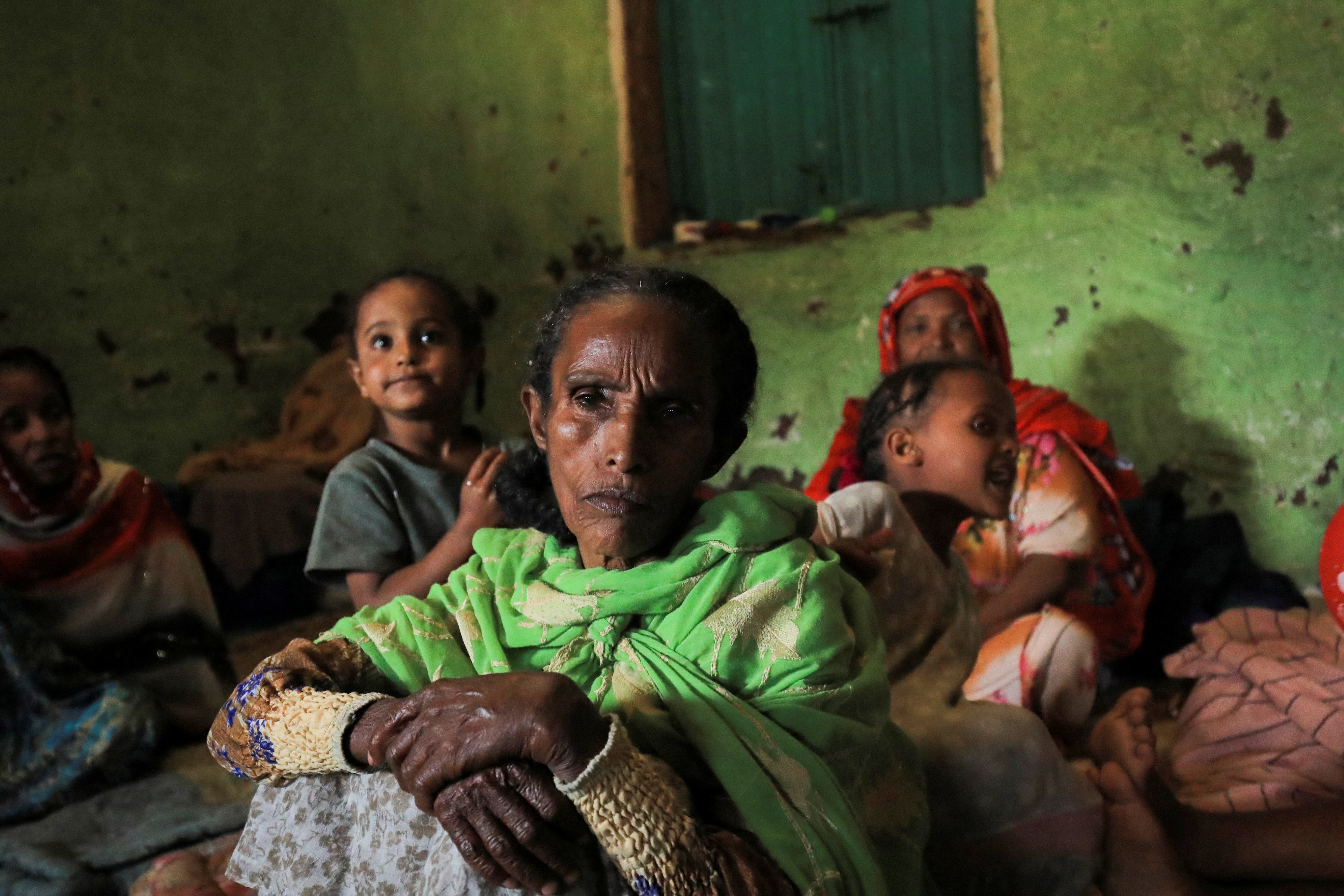 An elderly woman and her family sit in a shelter at a camp for displaced people