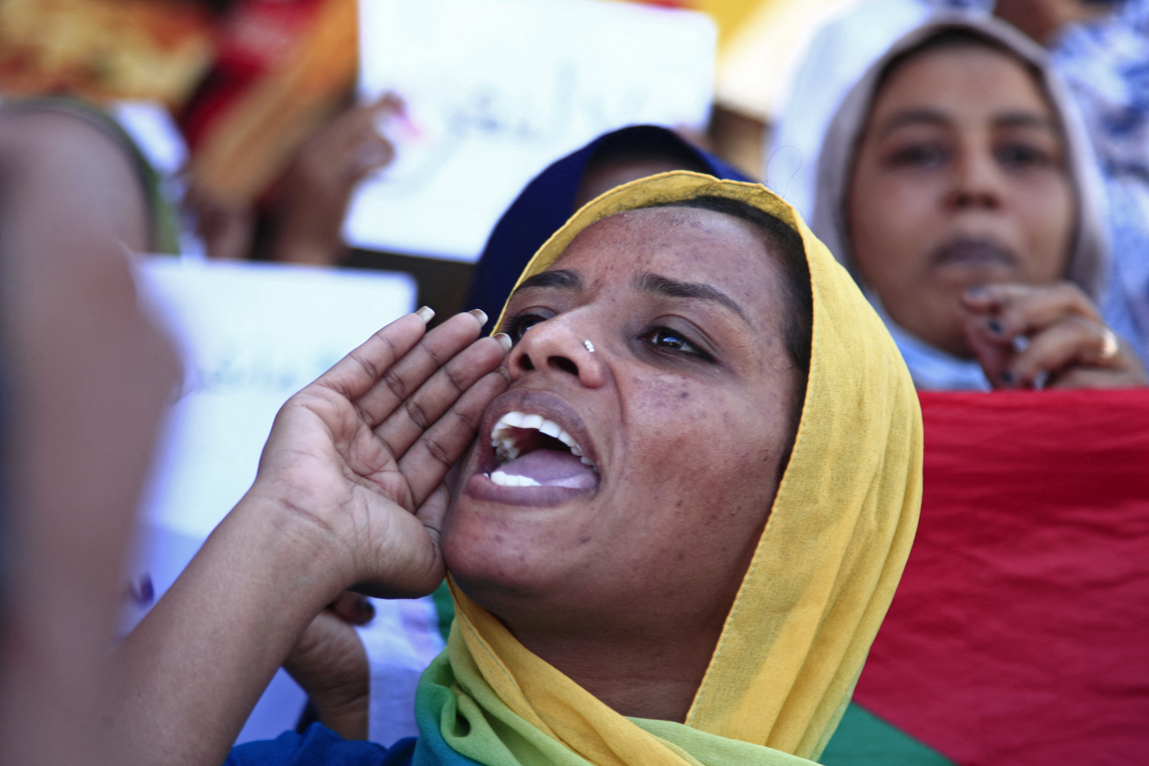 A woman in a yellow scarf shouts at a protest.