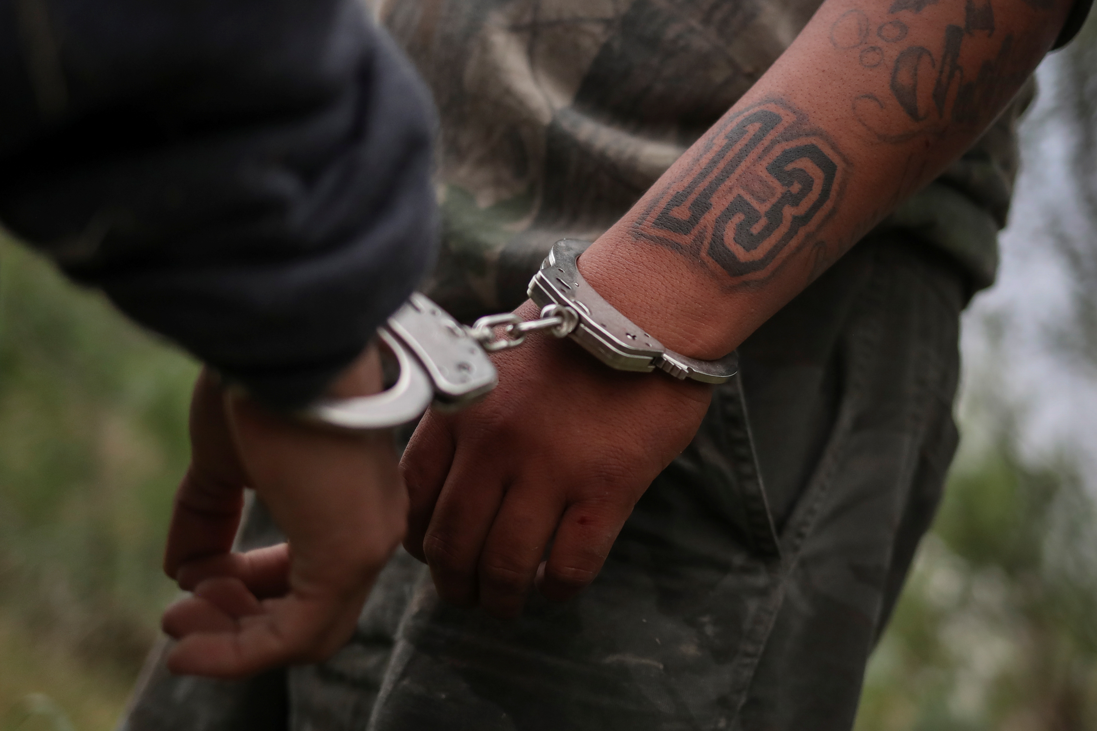 A migrant from Central America, is handcuffed by border patrol agents who suspected he was a member of the gang Mara Salvatrucha (commonly known as MS-13) [File: Adrees Latif/Reuters]