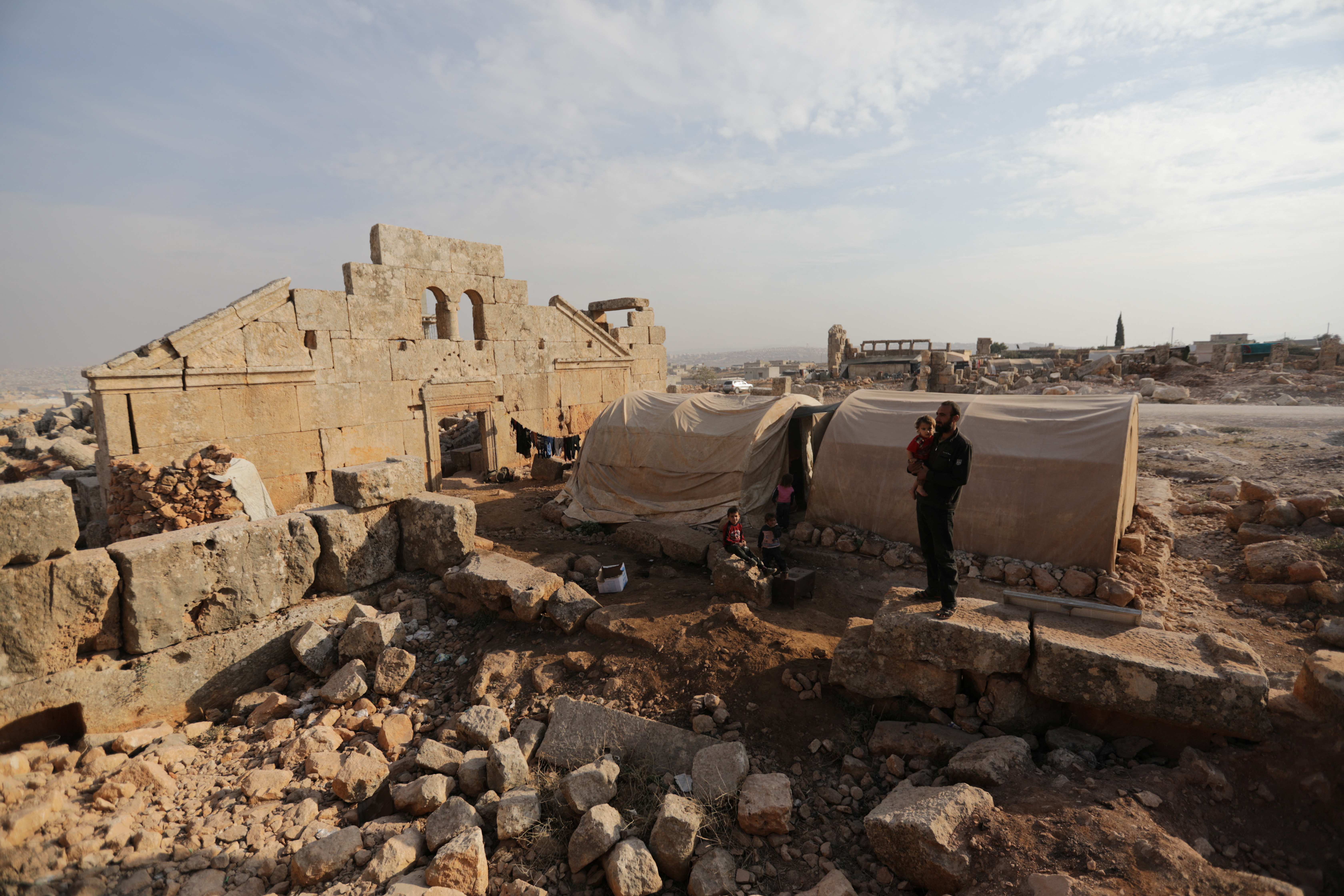 Mohamad Othman, 30, stands with his children beside their tent in the archaeological site of Sarjableh, Syria