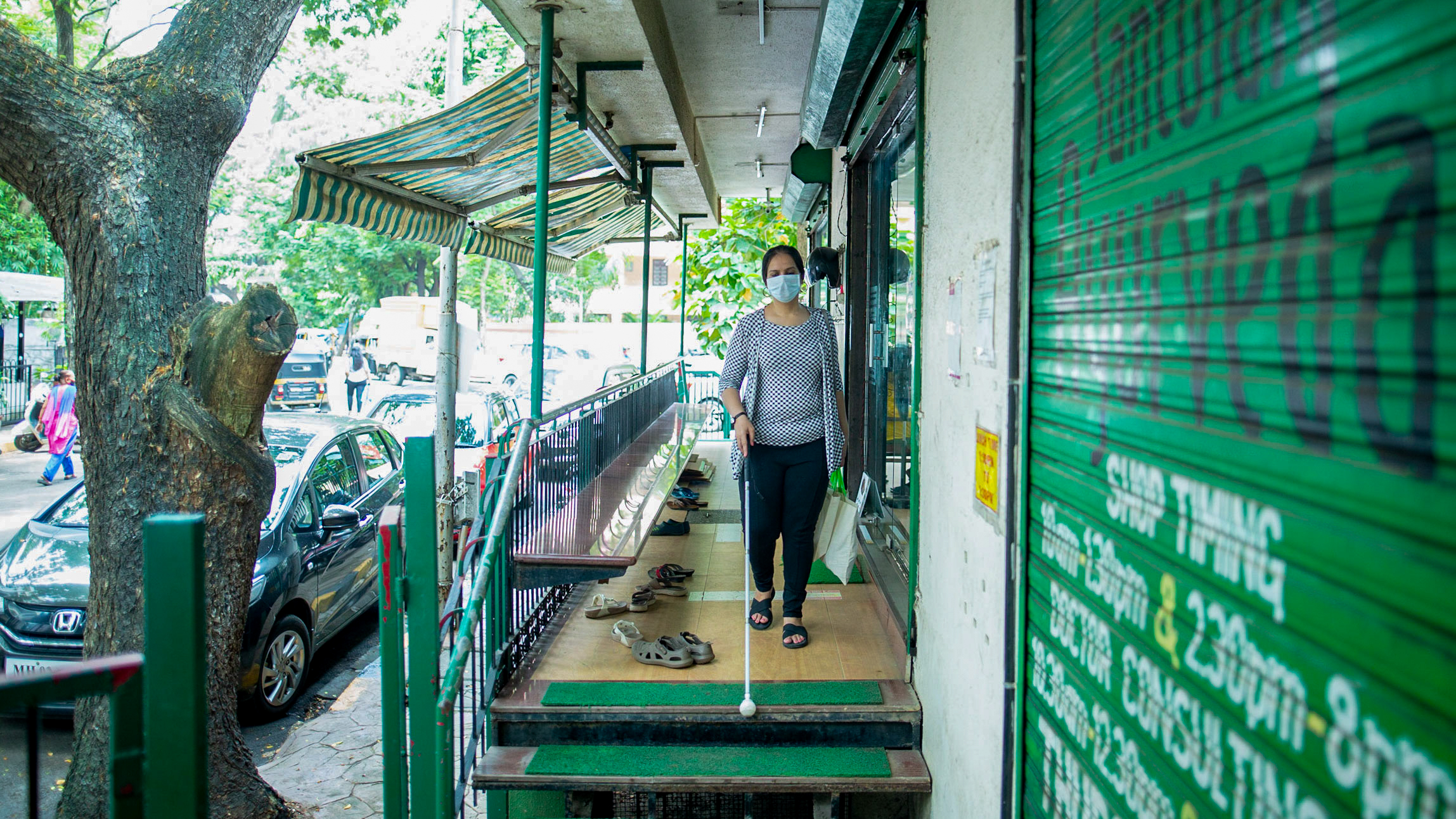 Nidhi, a 36-year-old woman, with a couple of shopping bags walks down the stairs using her white cane.