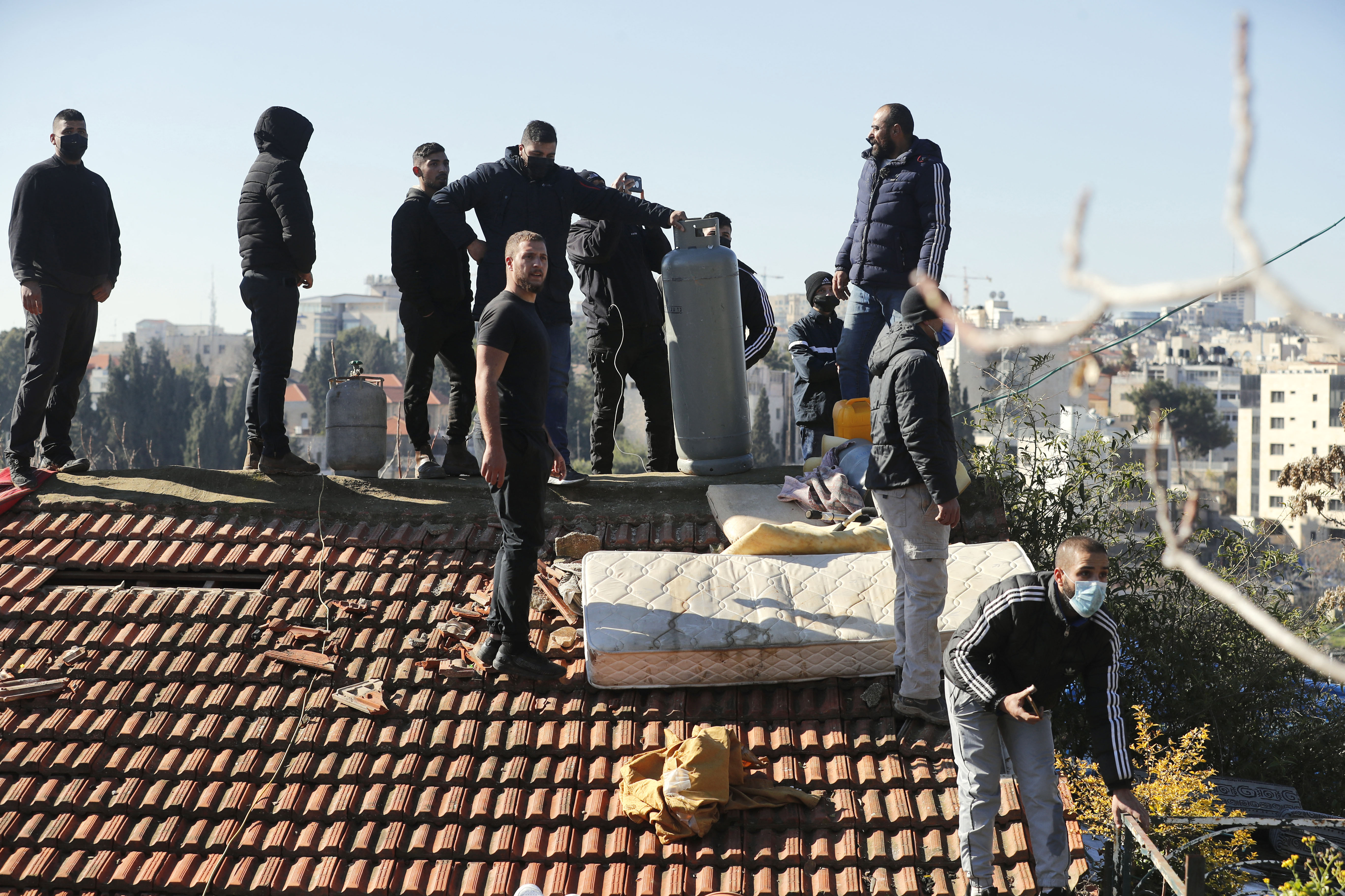 Palestinian men hold a gas tank on the roof of their house