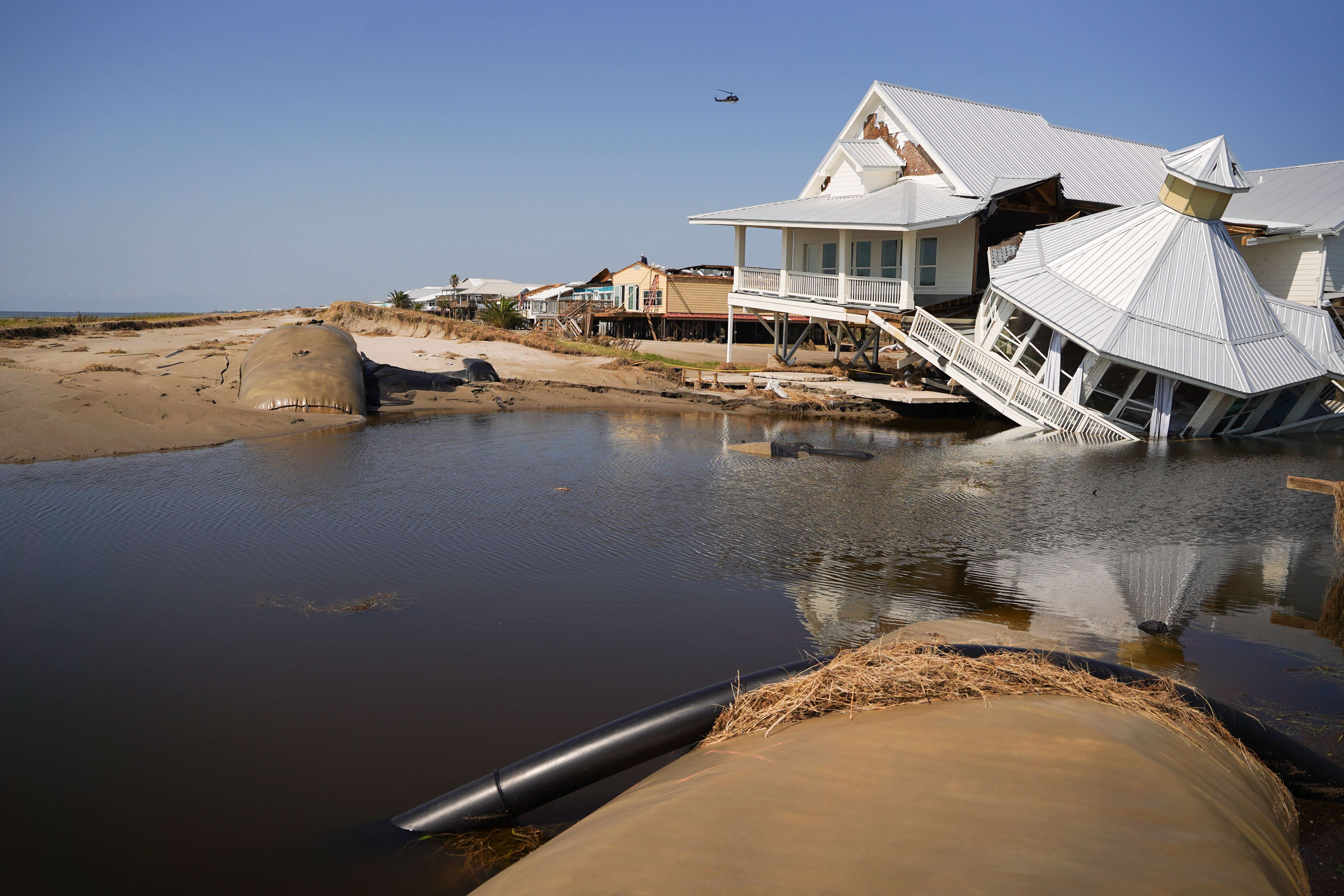 A photo of a house by the sea that has been damaged with half of the house upright and the other half broken and falling into the water.