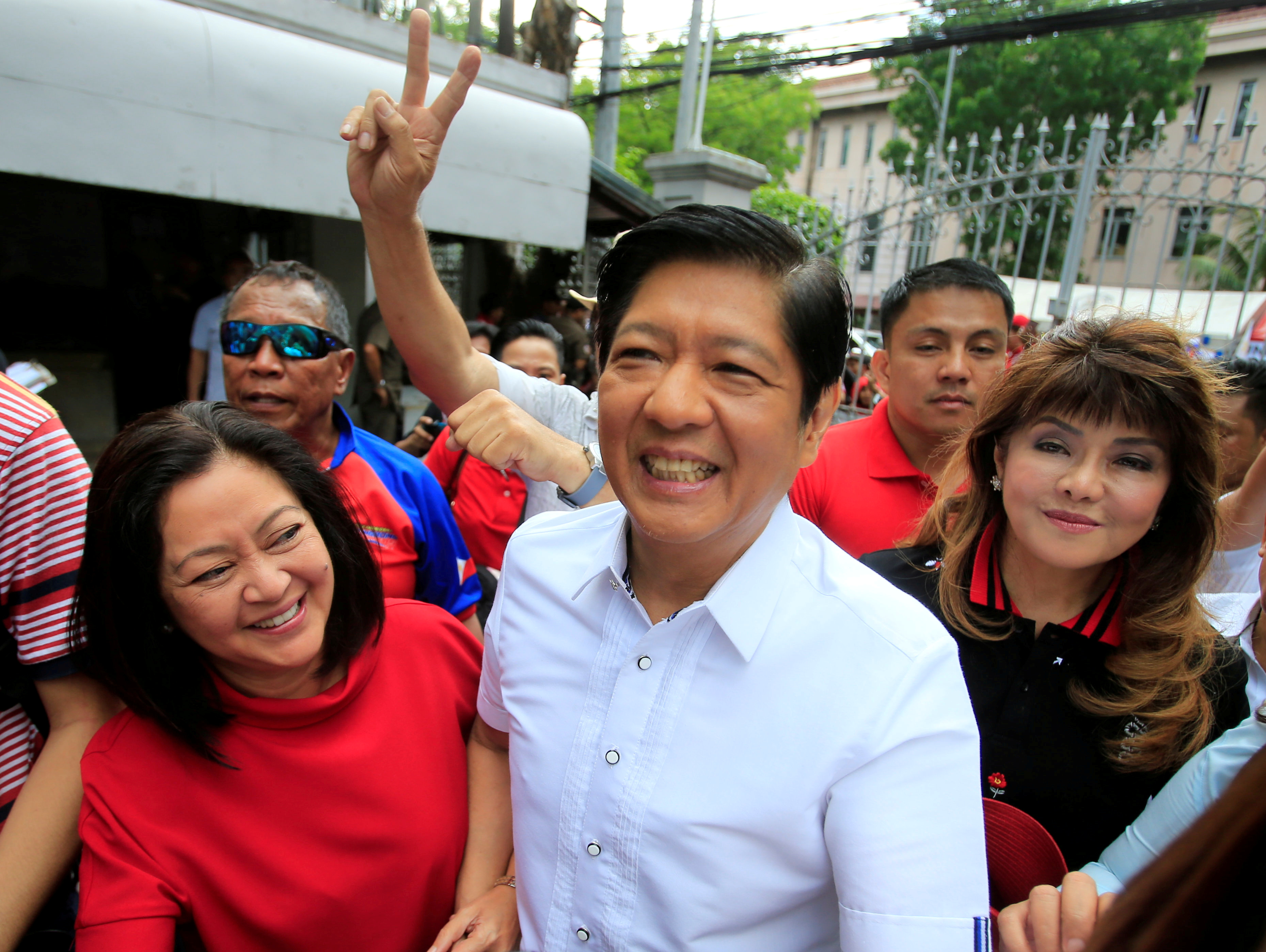 'Bongbong' Marcos in a white shirt and accompanied by his wife and sister smiles to a crowd.