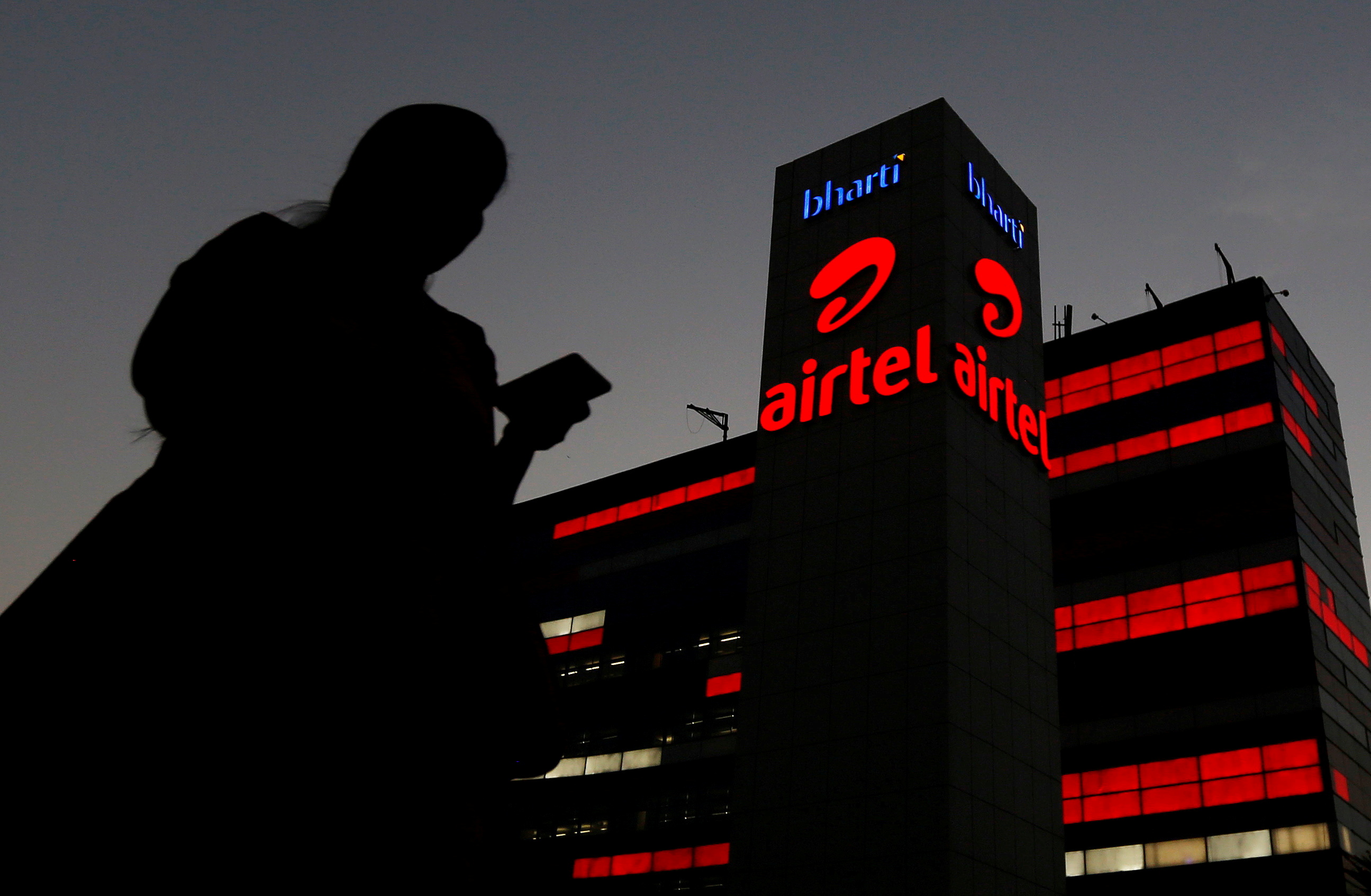 A girl checks her mobile phone as she walks past the Bharti Airtel office