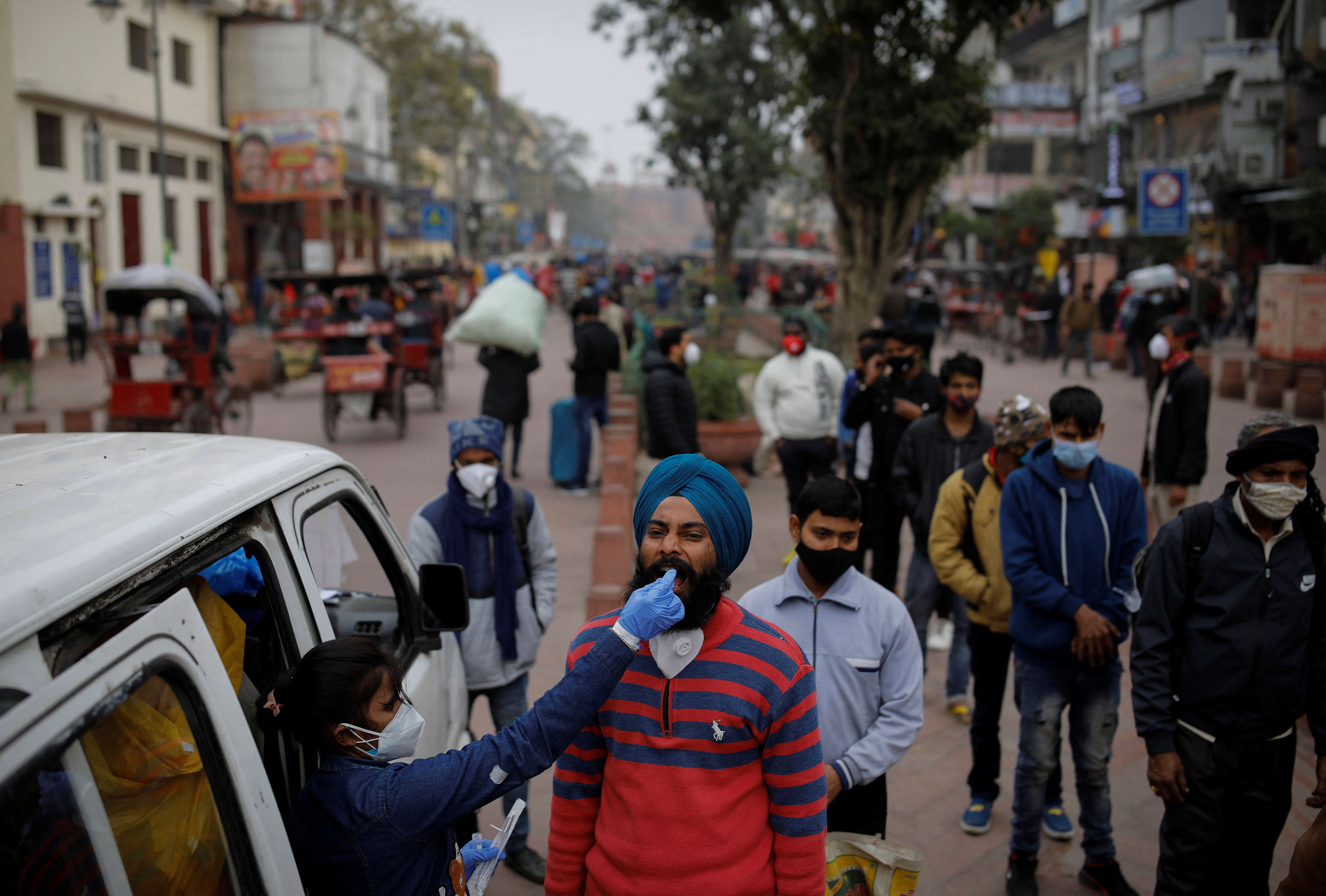 A healthcare worker collects a COVID-19 test swab sample from a man in Delhi, India