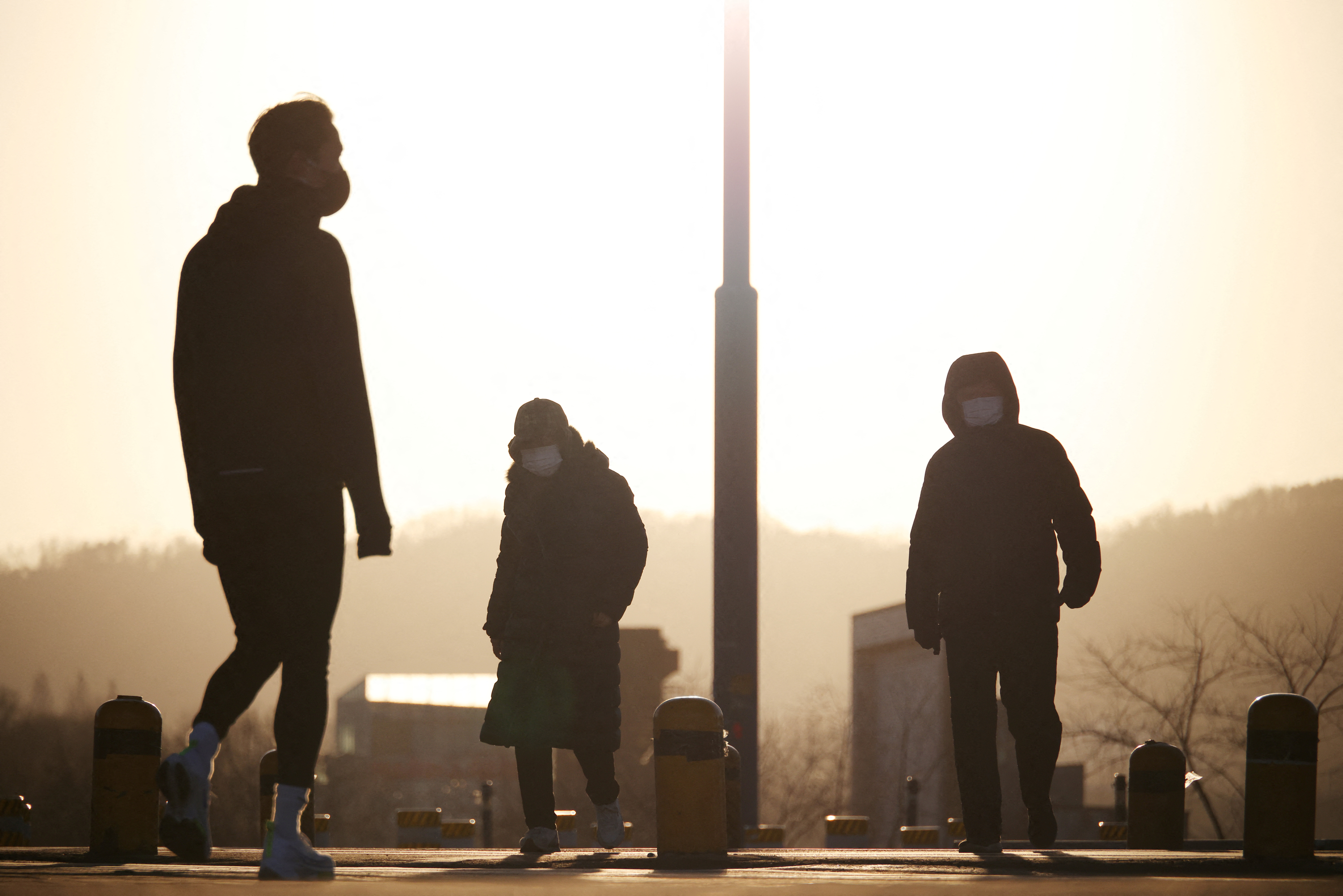 Three people wearing masks silhouetted against the sky on a cold morning in Seoul