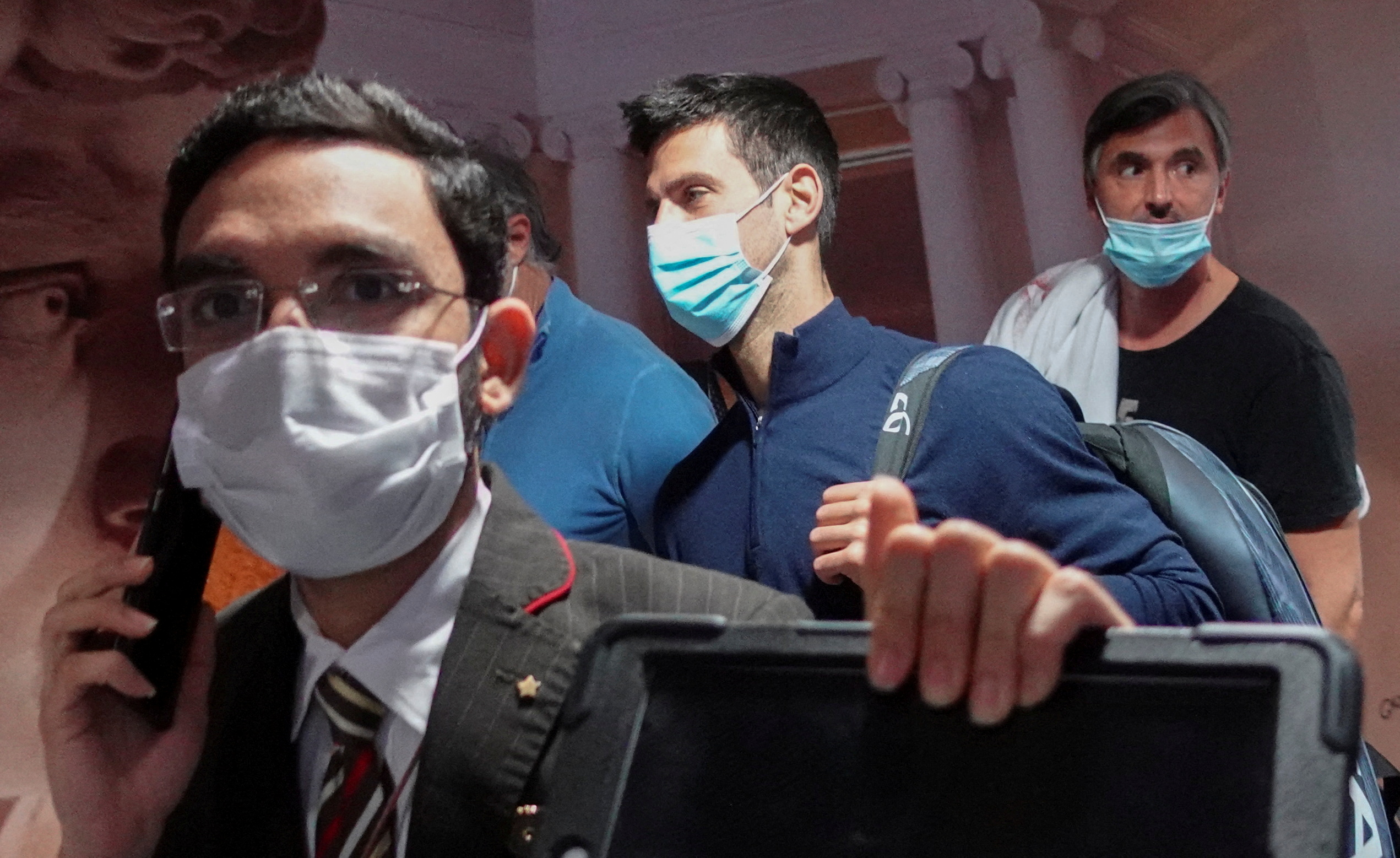 Novak Djokovic, masked and in a blue shirt, gets off the plane with his team in Dubai after being deported from Australia