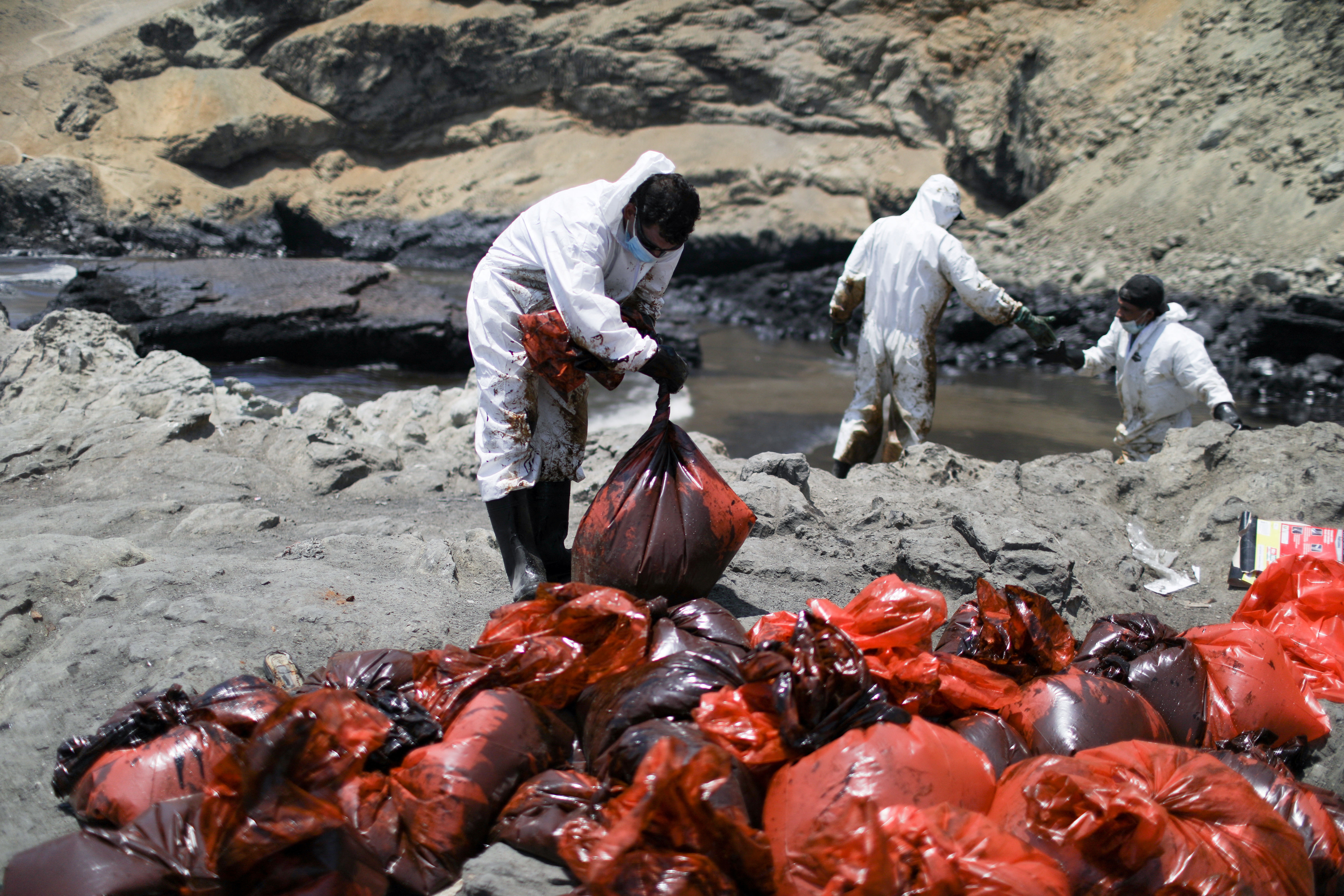 Workers clean up an oil spill caused by abnormal waves in Ventanilla, Peru