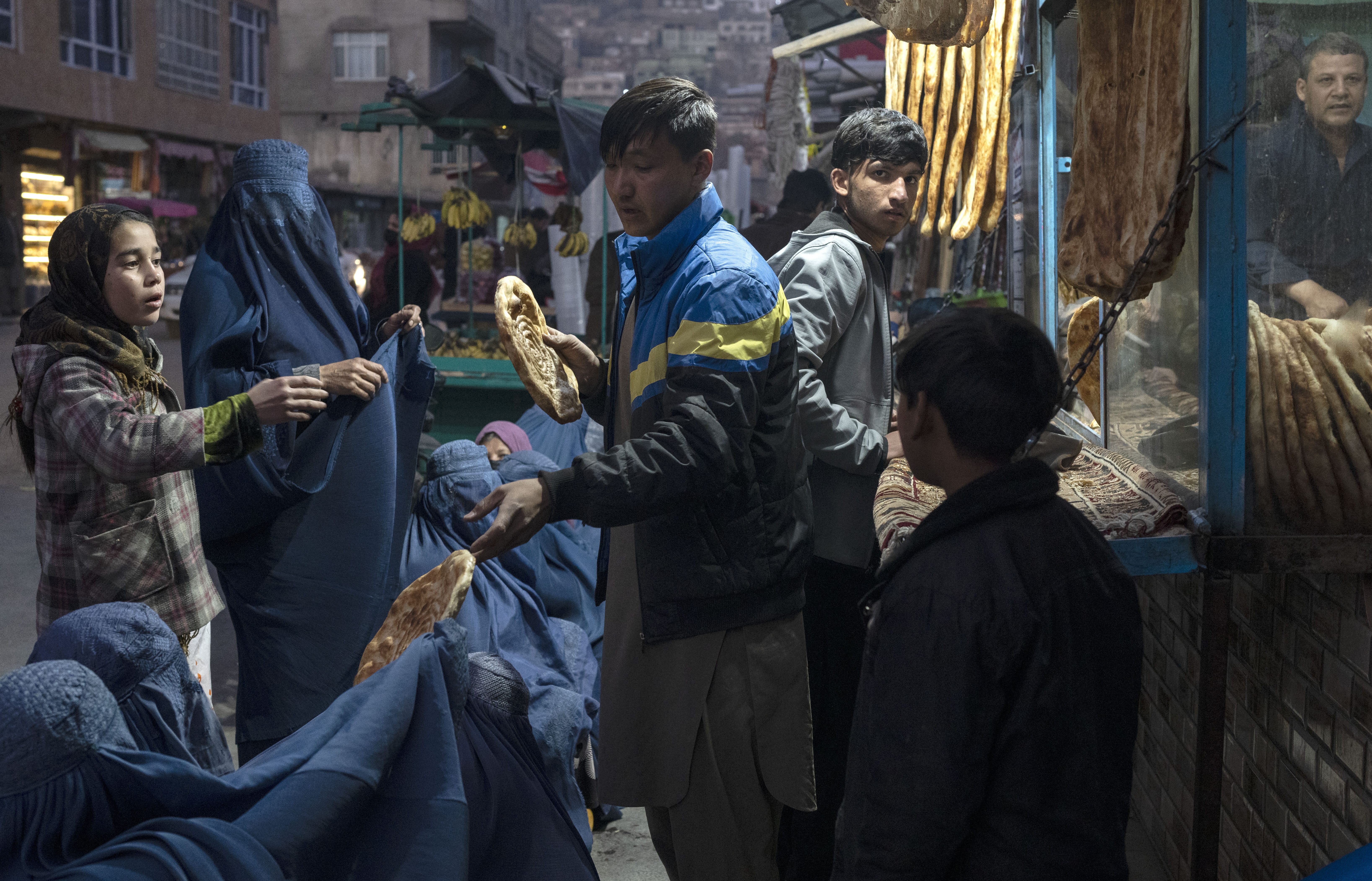 A man disributes bread to Afghan women outside a bakery in Kabul