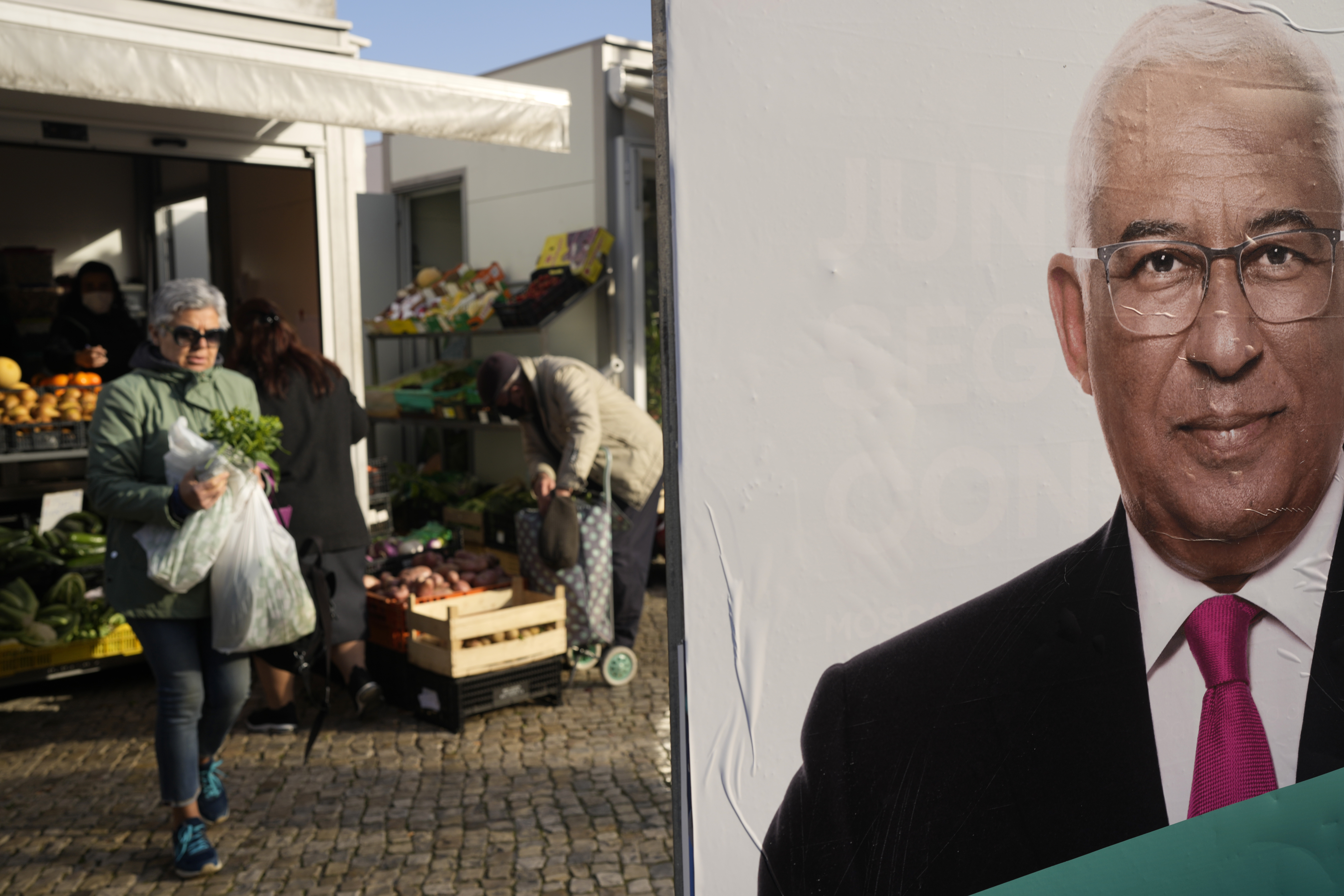 People buy groceries next to an election campaign poster of Portuguese Prime Minister and Socialist Party Secretary General Antonio Costa