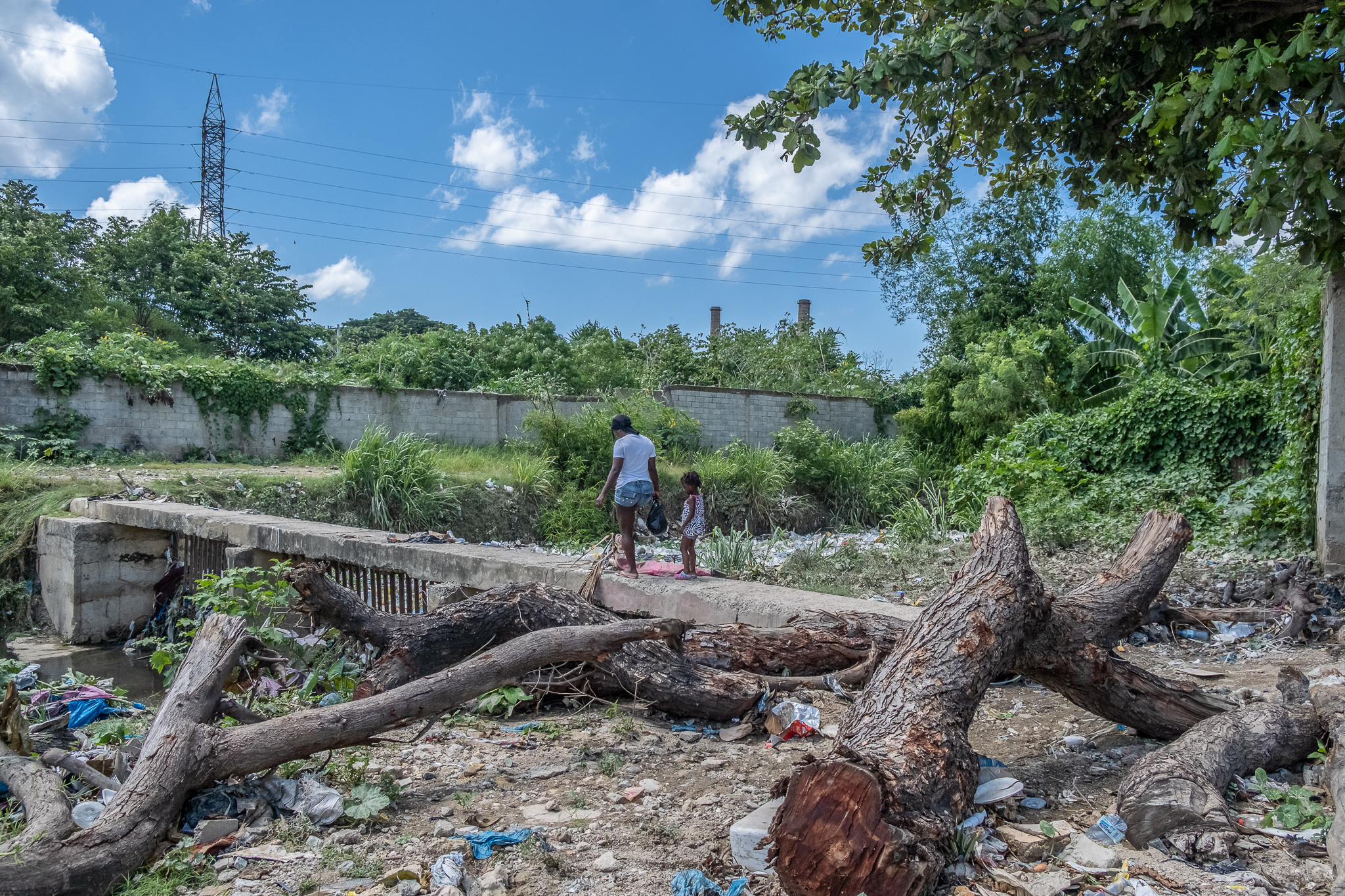 A woman and girl cross a bridge surrounded by trash