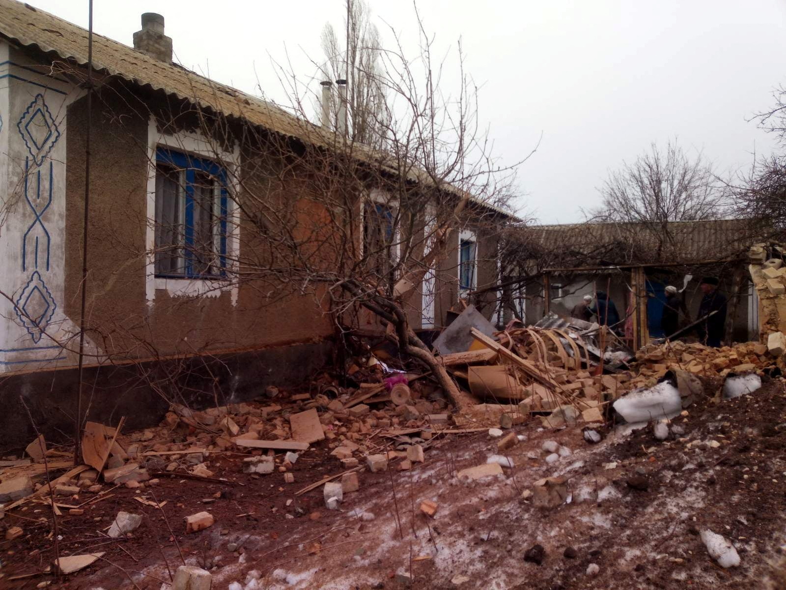 Local residents stand next to a building, which according to Ukraine's local officials was damaged by shelling, in the town of Vrubivka