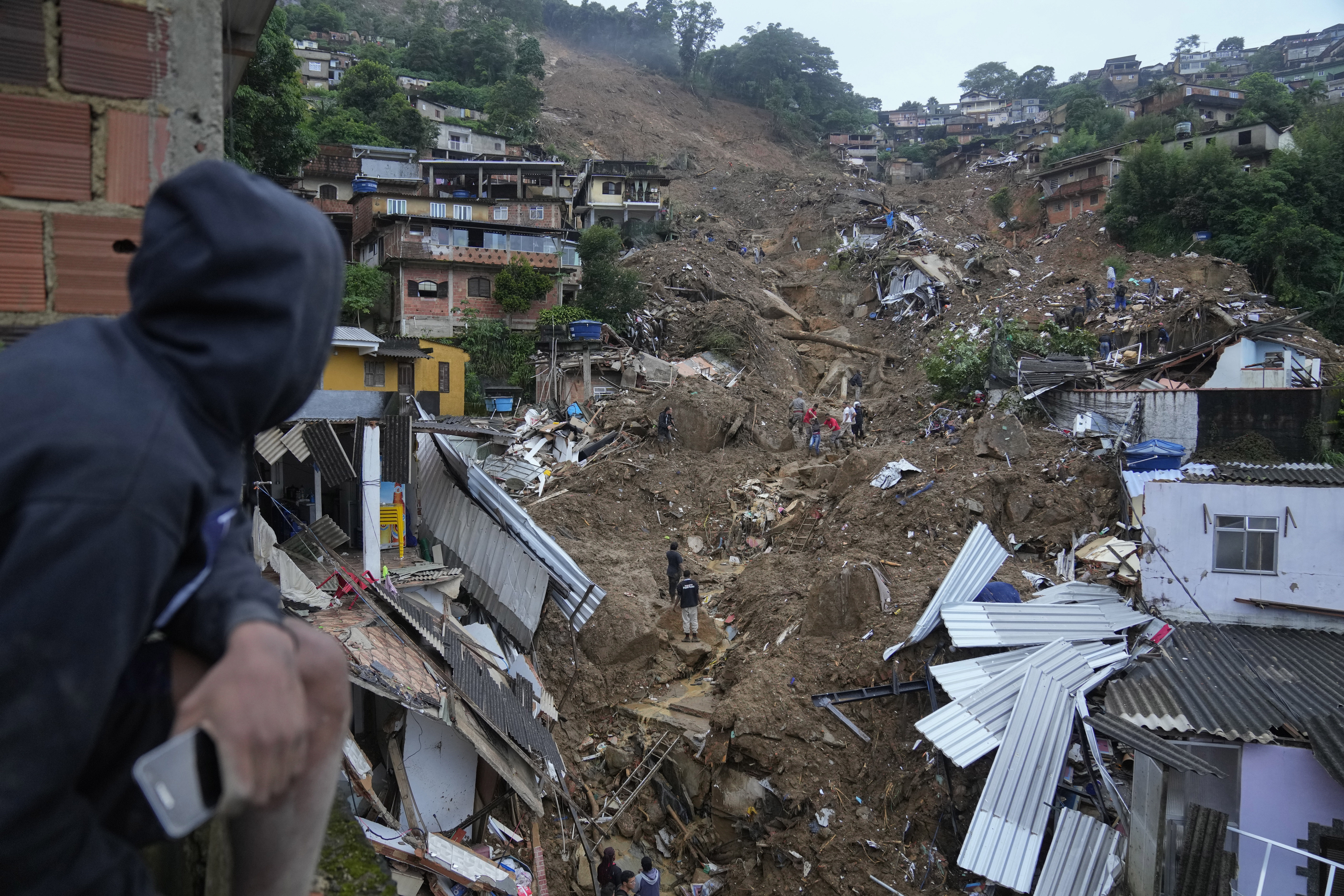 two residents look out on the landslide that tore down the hill burying homes and uprooting trees