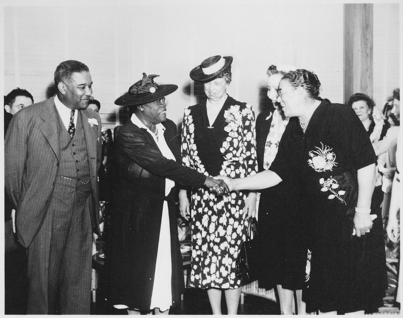 Two women shake hands as other people look on