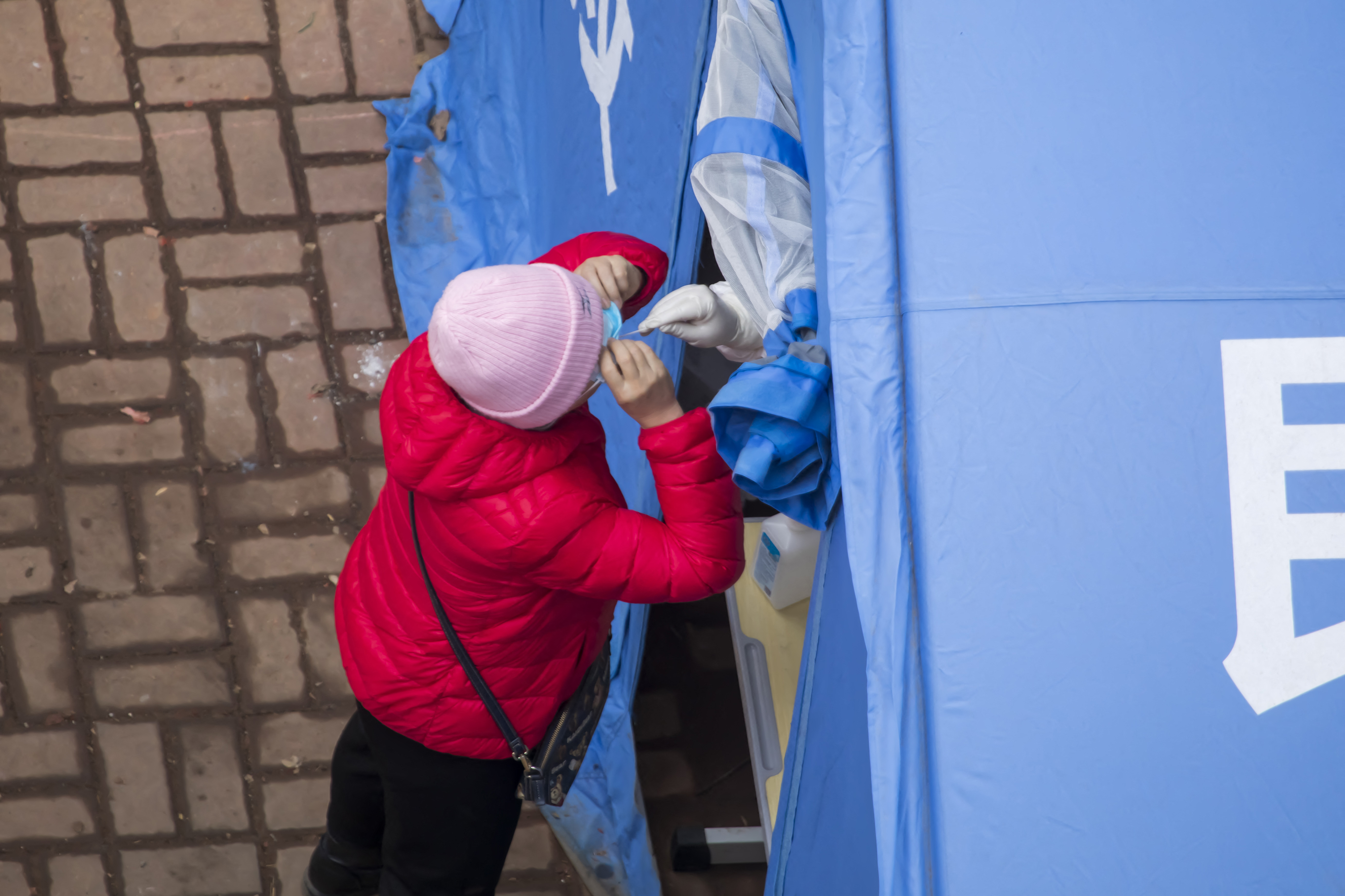 A woman in a red coat and pink hat endures a nasal swab during mass testing for residents of Jilin