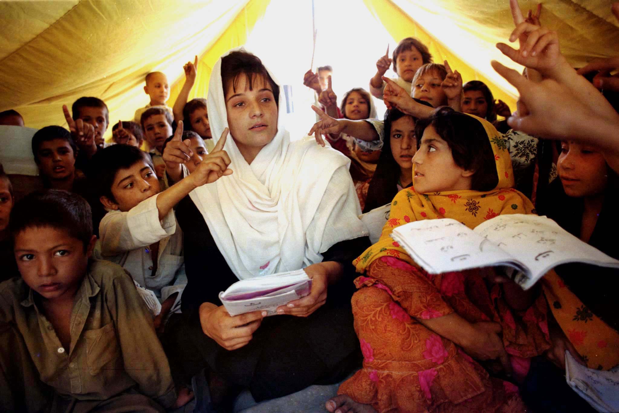 Afghan pupils sitting around their teacher (C) raise their hands to answer a question during a class in a tented school October 10, 1996