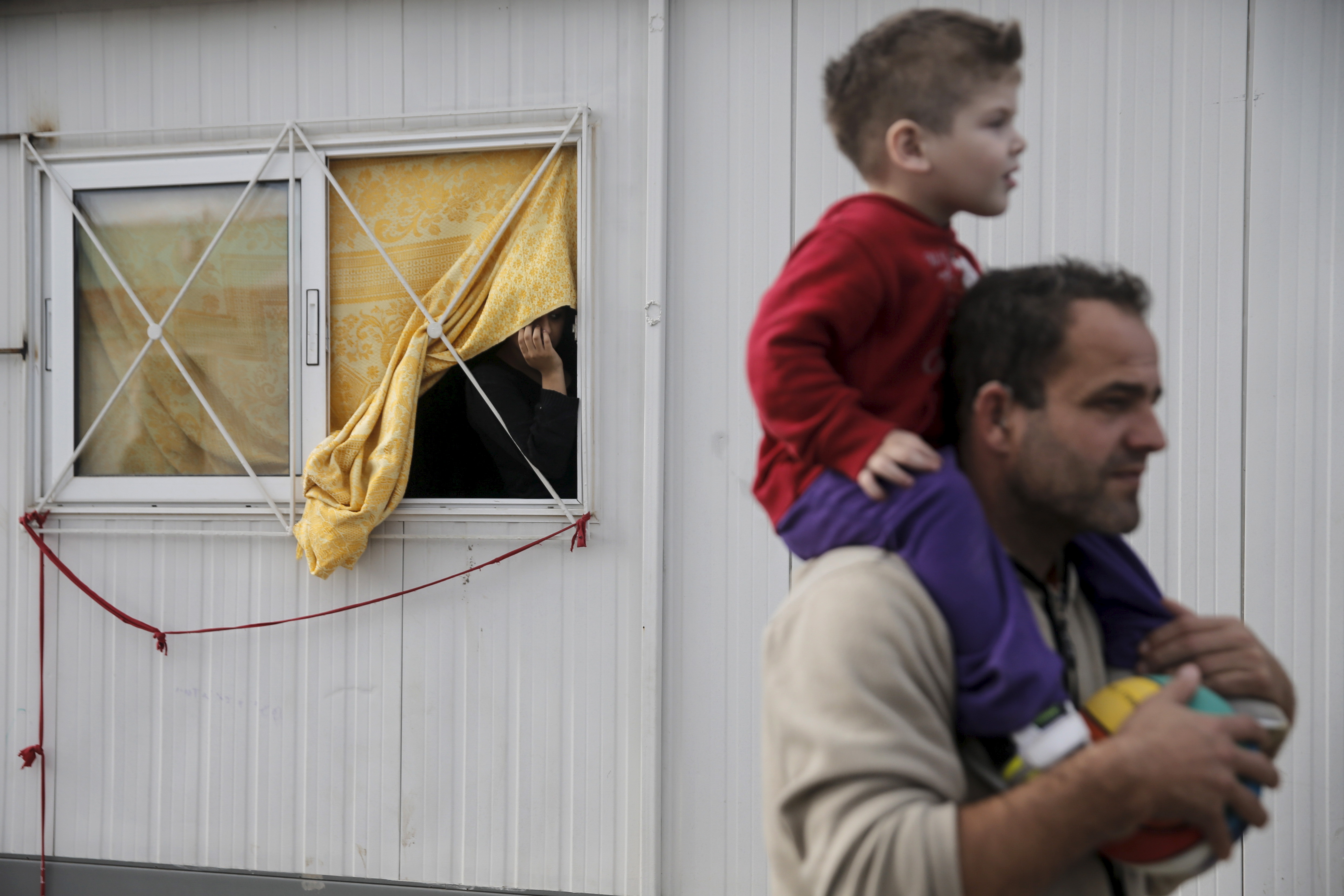 A refugee (L) looks through a window at the Eleonas refugee camp in Athens, Greece, January 5, 2016. REUTERS/Alkis Konstantinidis