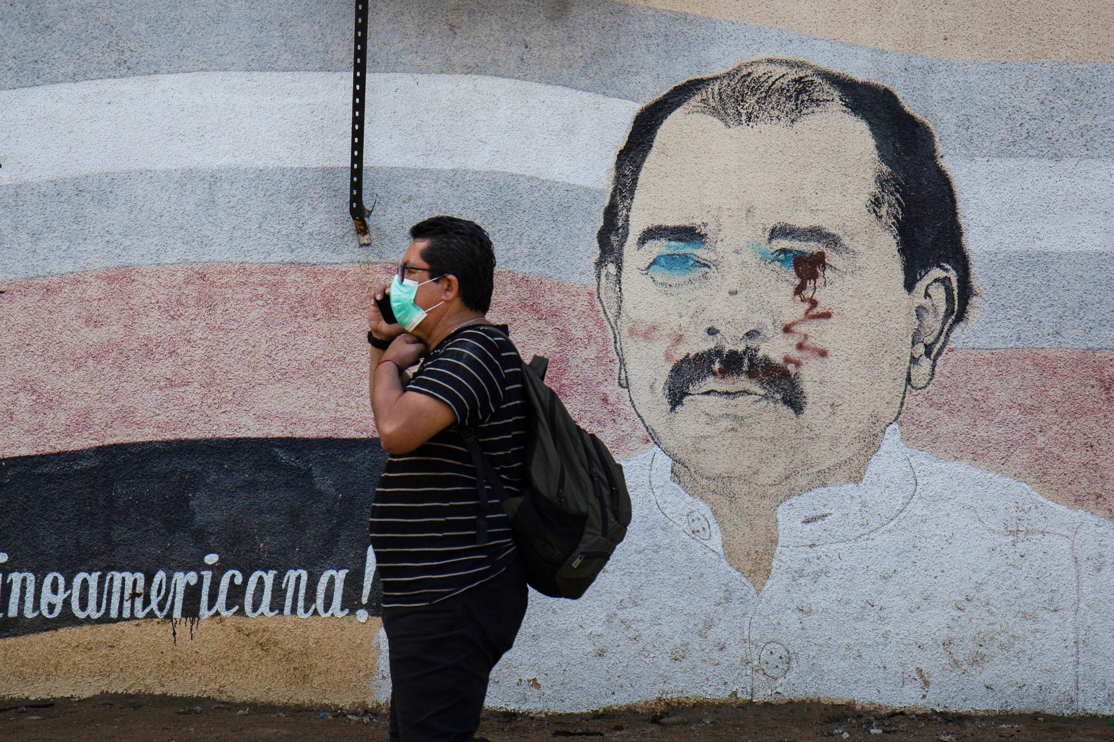 A man walks by a mural of Daniel Ortega