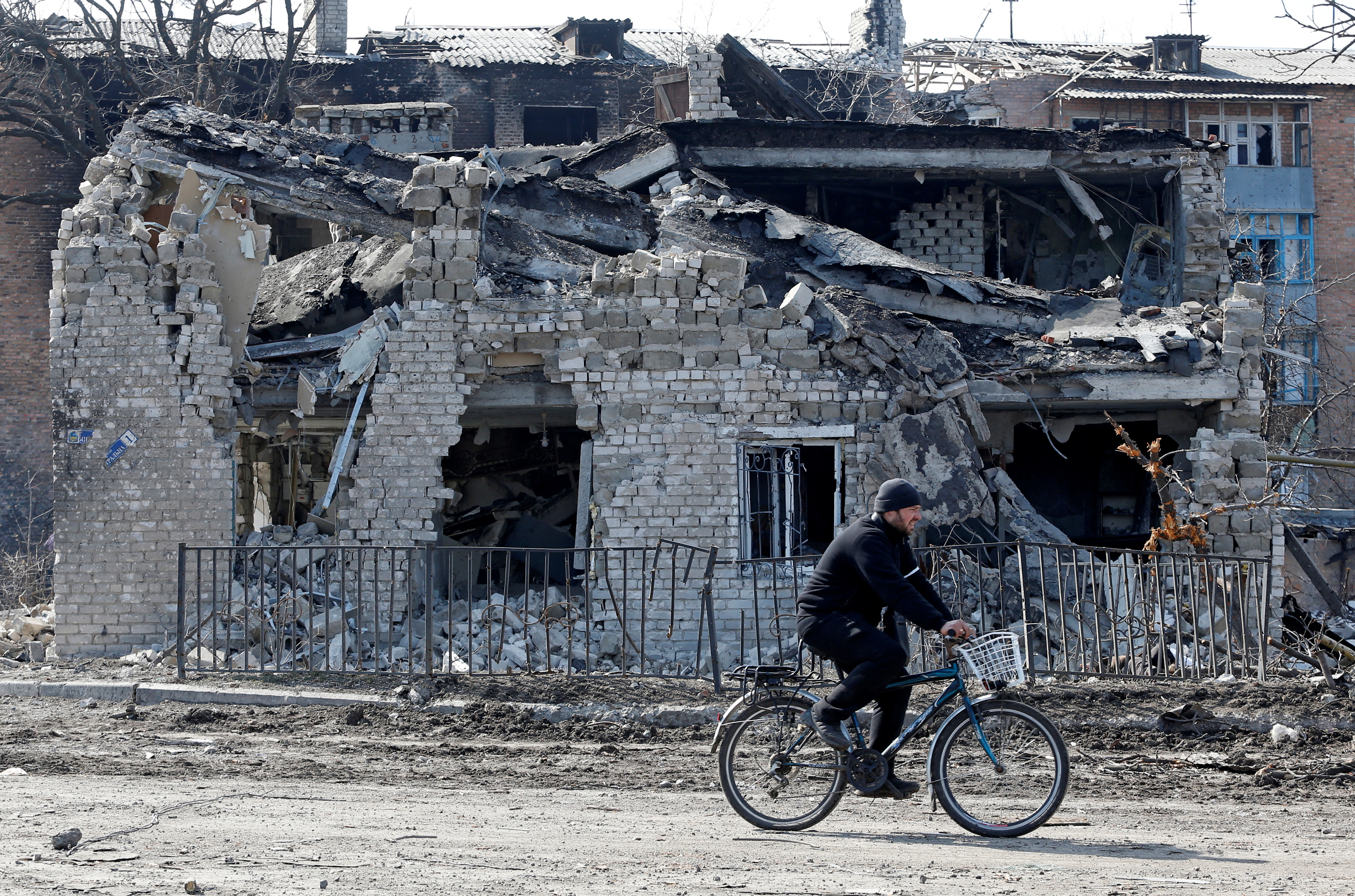 A local resident rides a bicycle past a destroyed building.