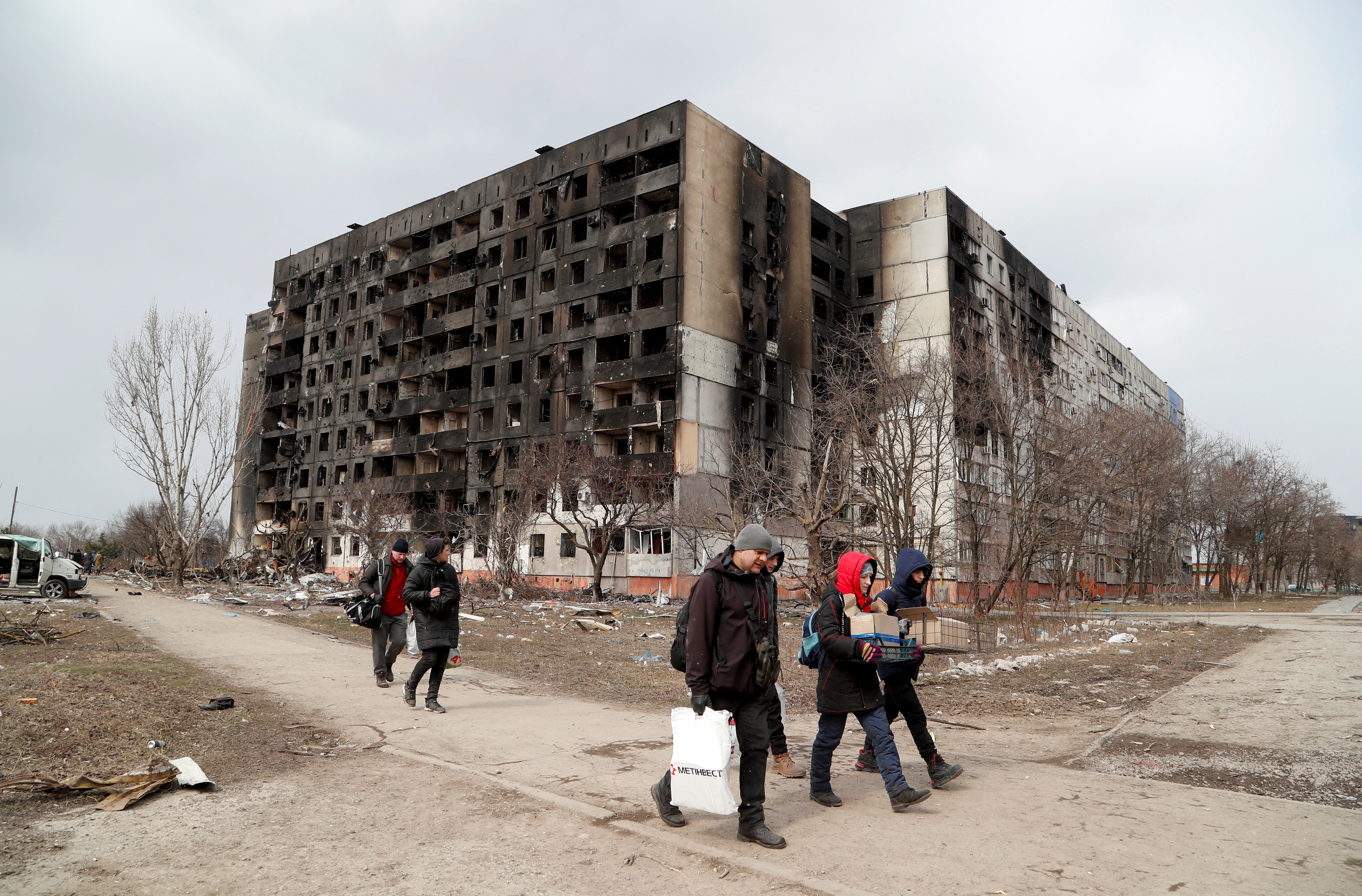 People walk along a street near a block of flats, which was destroyed during Ukraine-Russia conflict in the besieged port city of Mariupol,