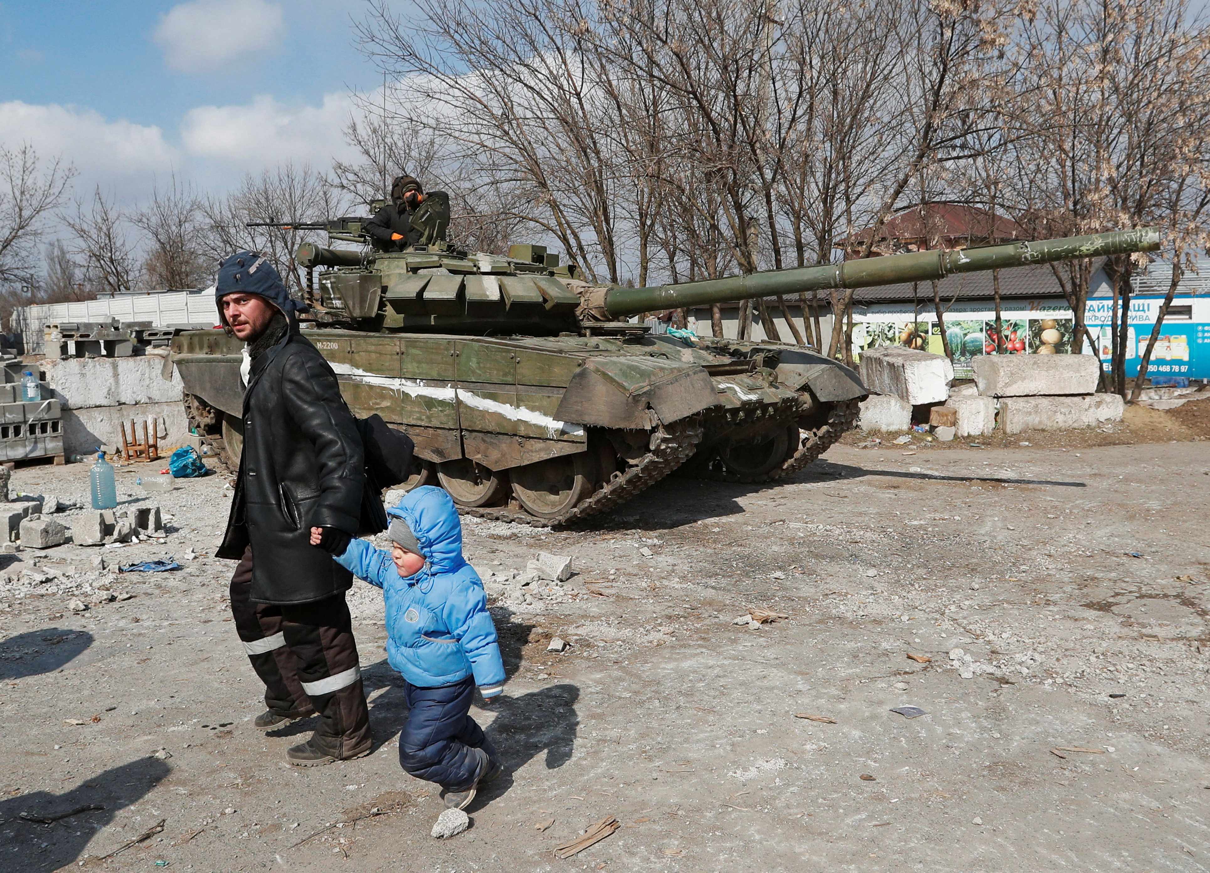 A local resident walks with a child past a tank of pro-Russian troops 
