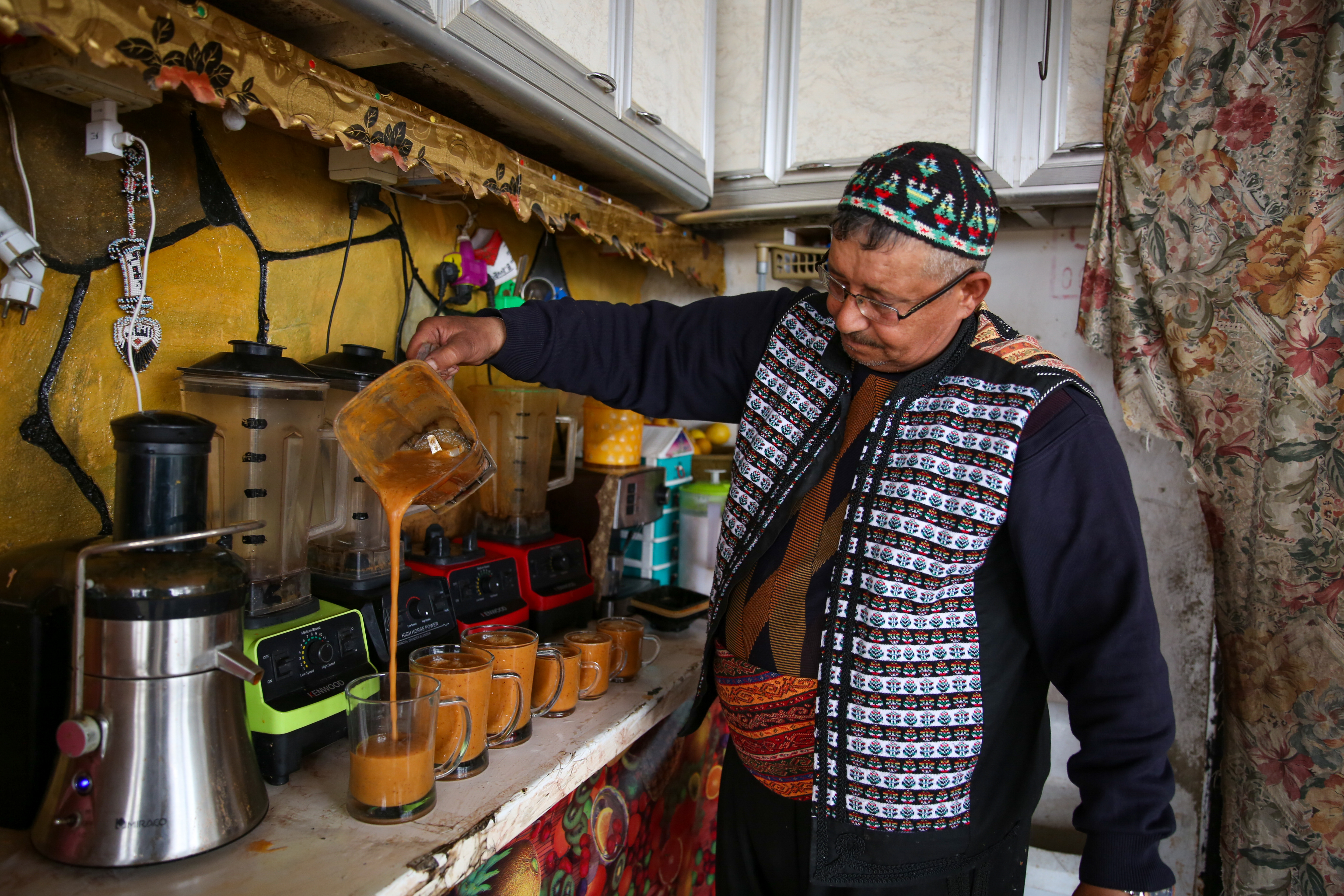 Safwan Daaboul pours a fruit cocktail drink out of a blender cup into a row of glasses