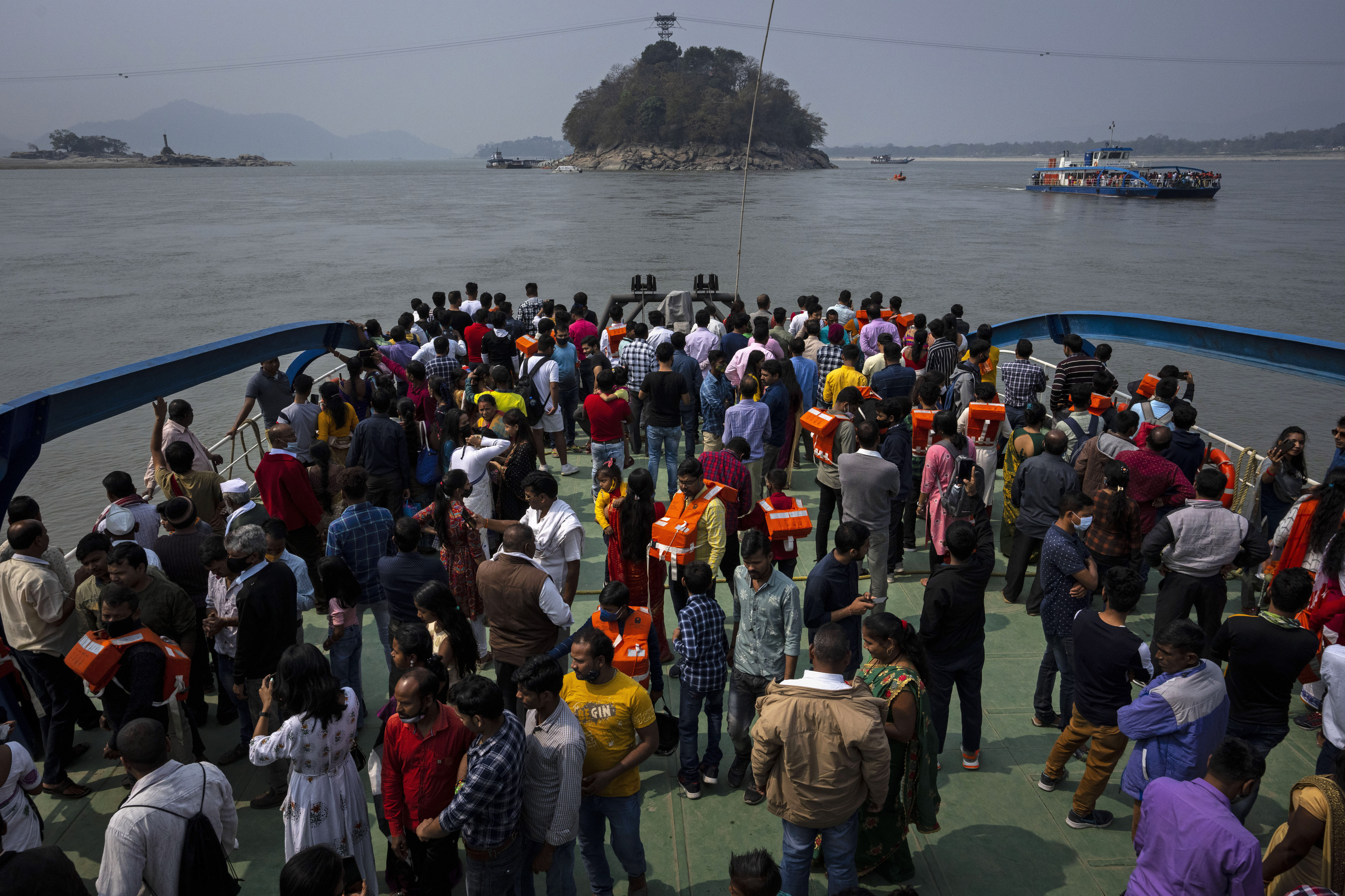 Devotees travel on a ferry to Umananda ,behind, a river island in the Brahmaputra that houses a temple of Hindu god Shiva, during Shivratri festival, in Gauhati, India,