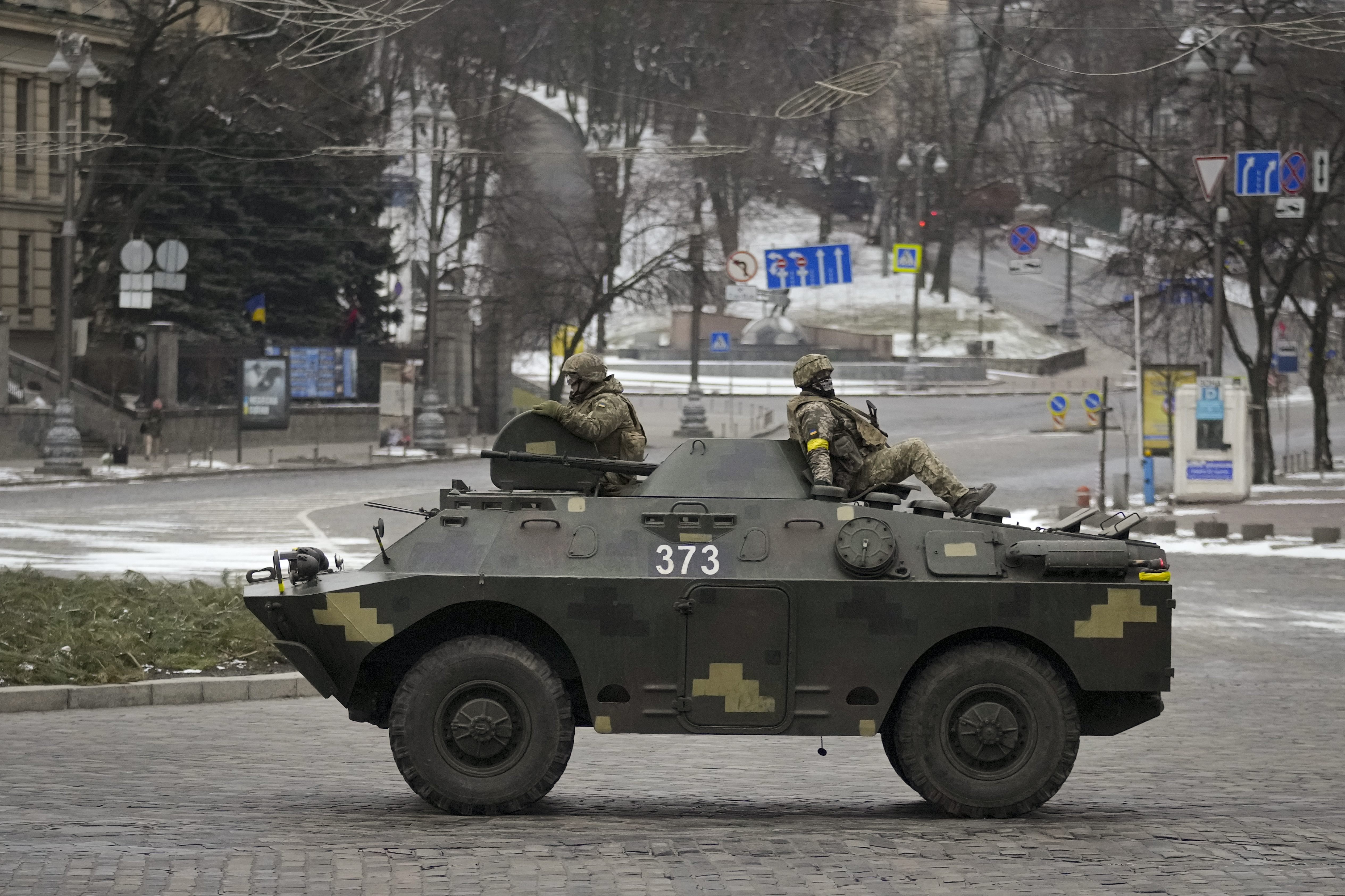 Ukrainian servicemen ride on top of an armored personnel carrier speeding down a deserted boulevard during an air raid alarm, in Kyiv