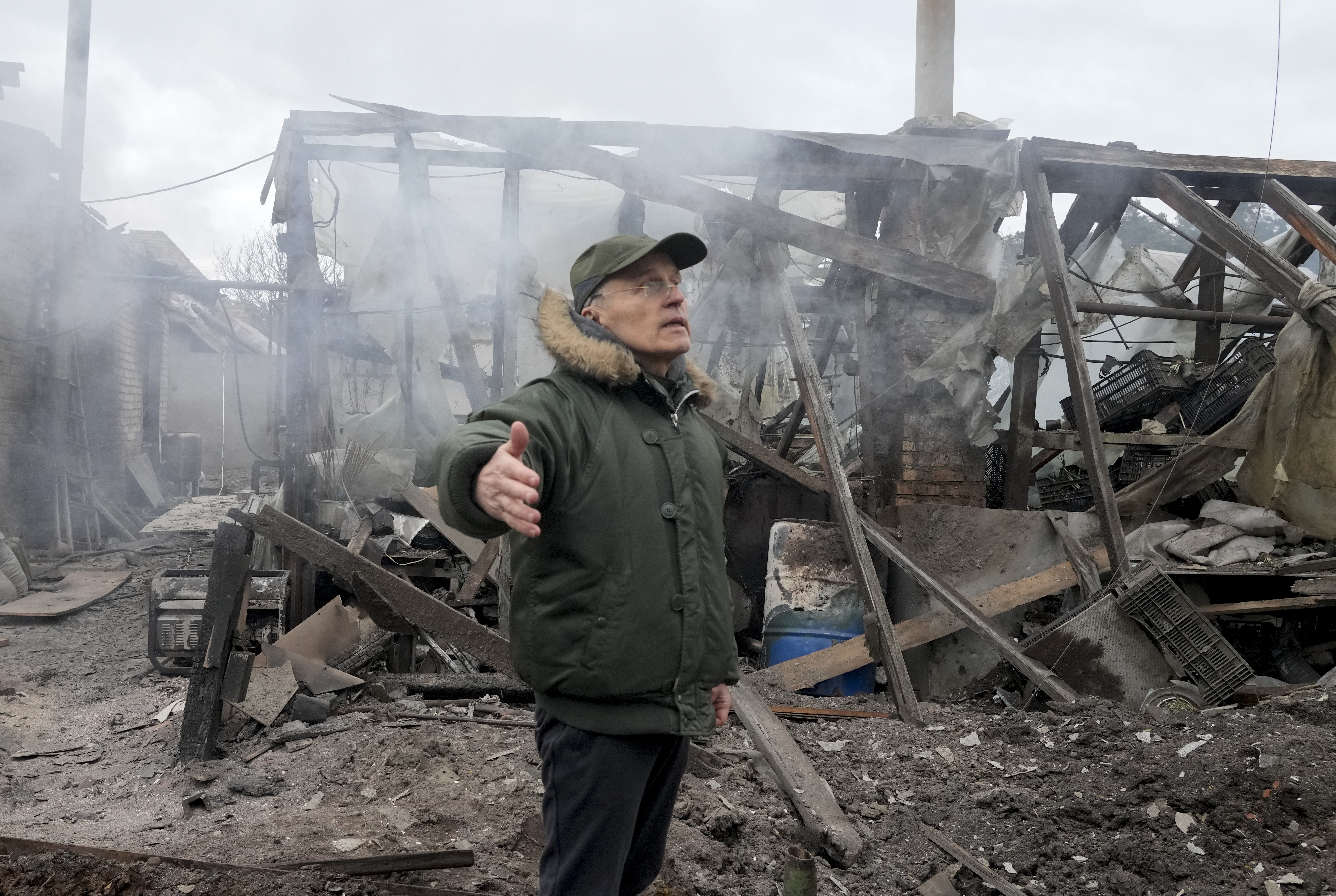 A man opens his arms as he stands near a house destroyed by Russian artillery shelling in Ukraine.