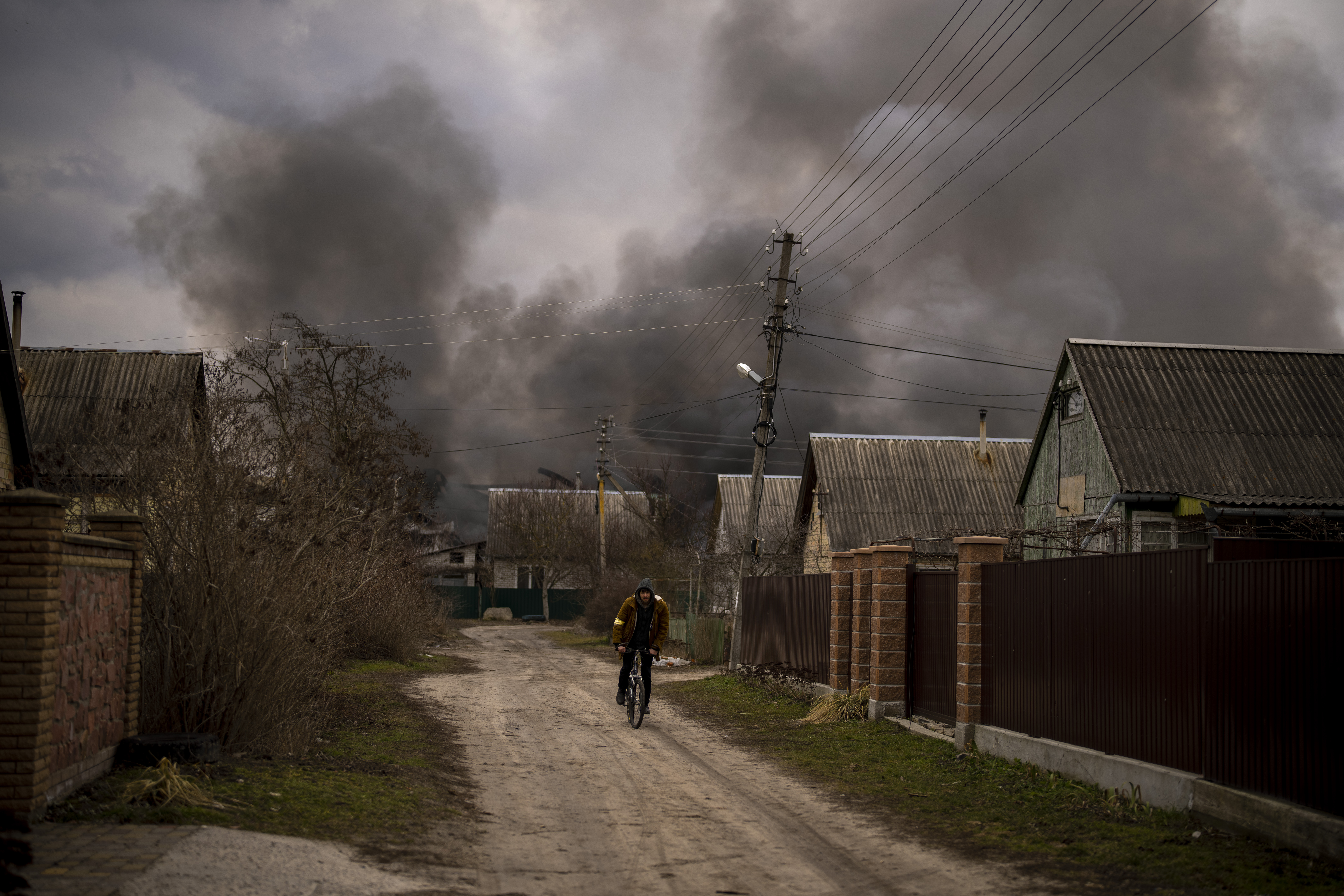 A Ukrainian man rides his bicycle near a factory and a store burning after they had been bombarded in Irpin