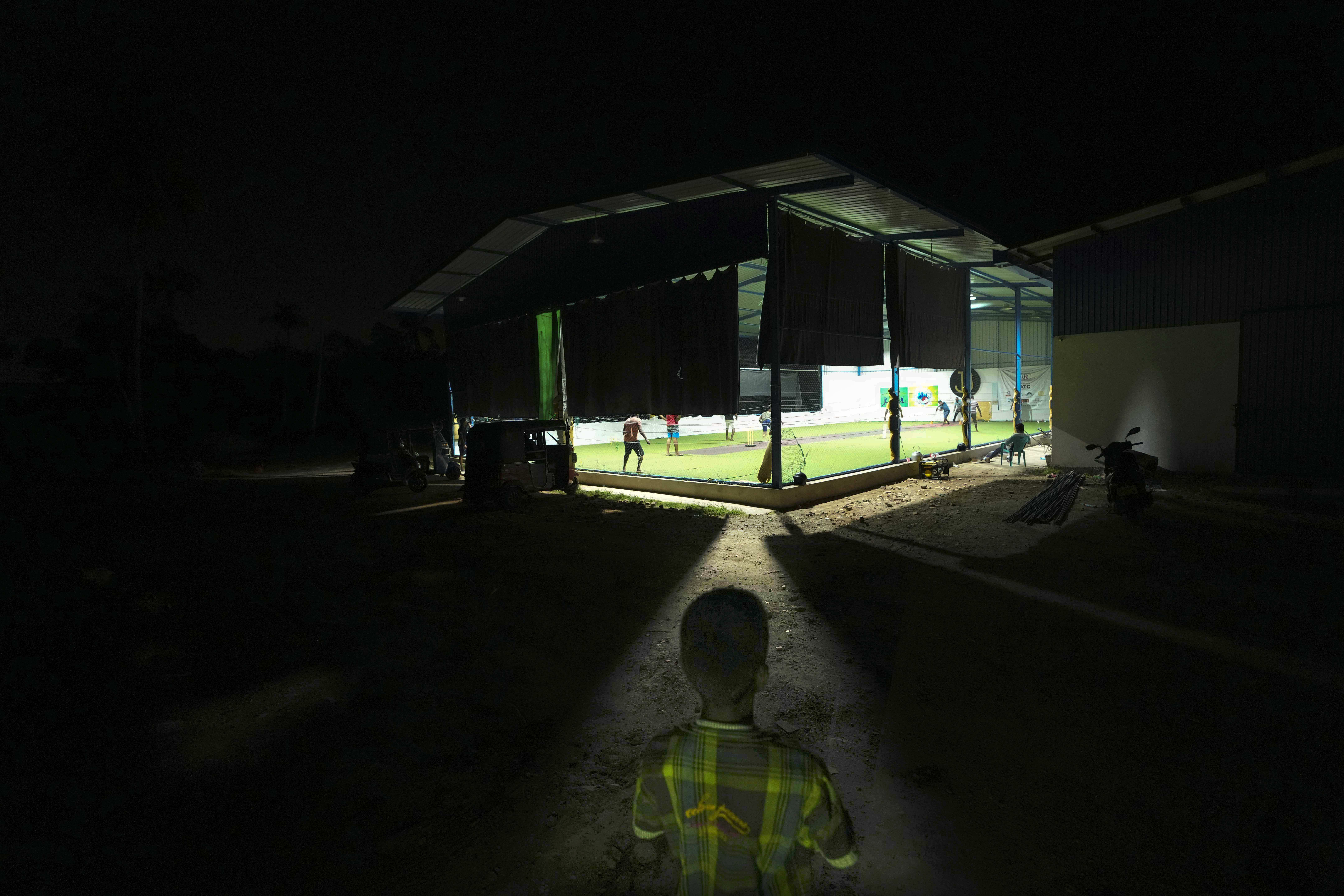 A Sri Lankan boy watches youth playing a pick up game of cricket