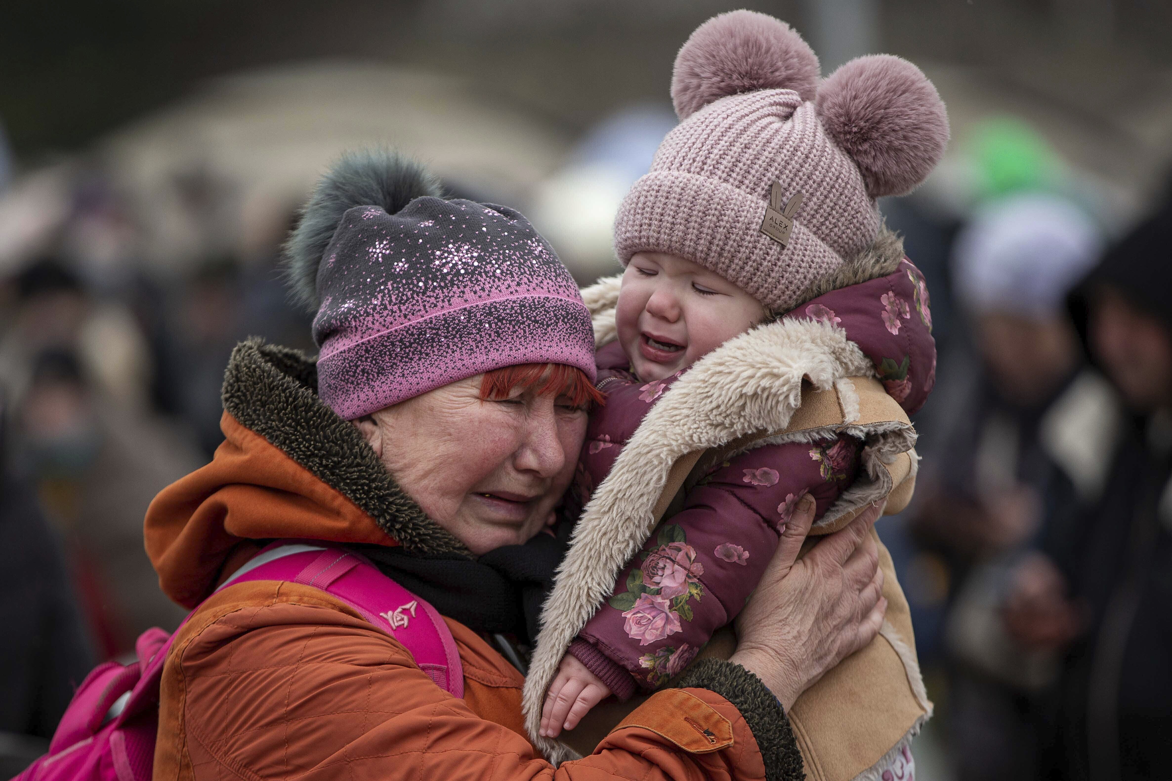 A woman holding a child cries after fleeing from Ukraine and arriving at the border crossing in Medyka