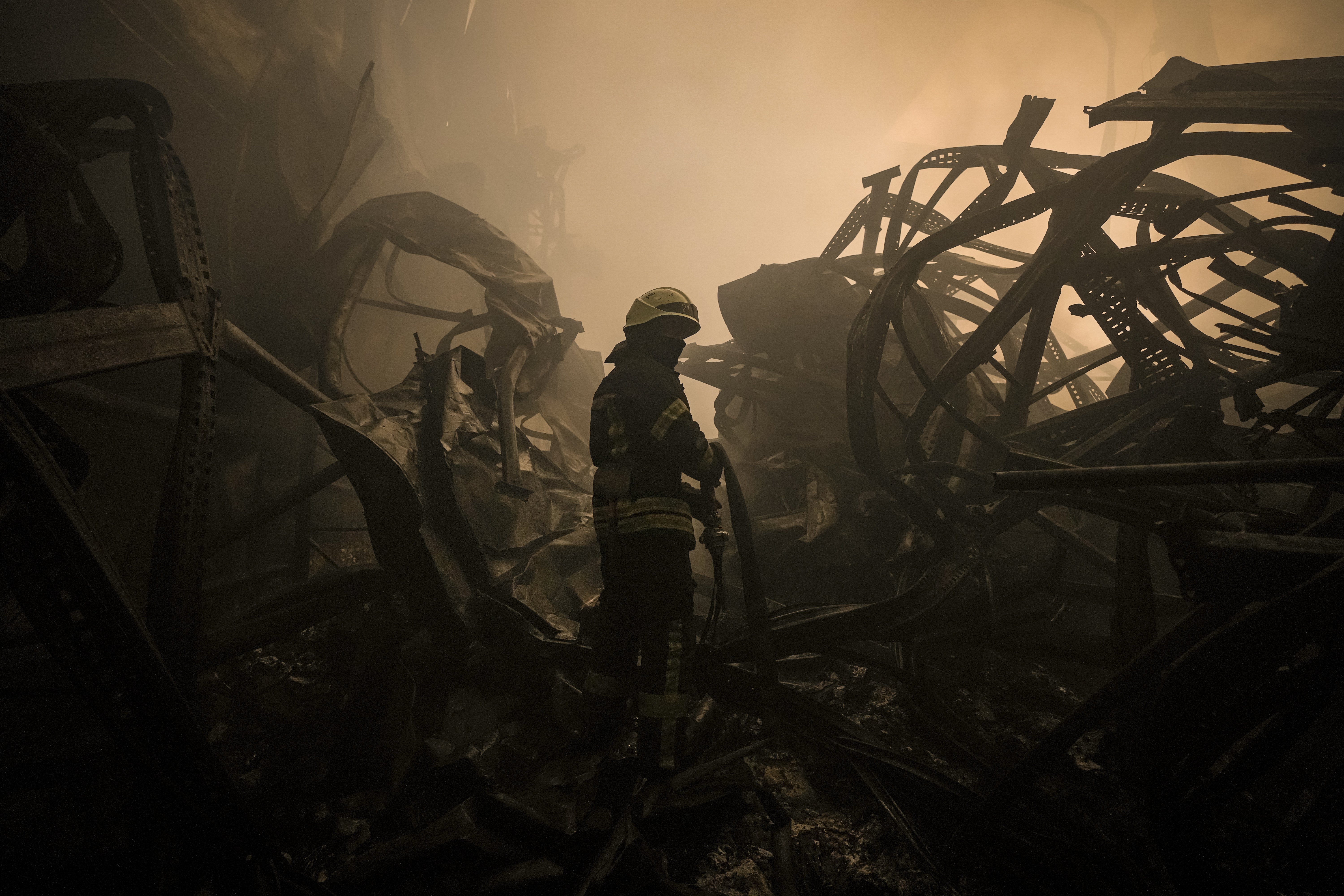 A Ukrainian firefighter drags a hose inside a large food products storage facility which was destroyed by an airstrike