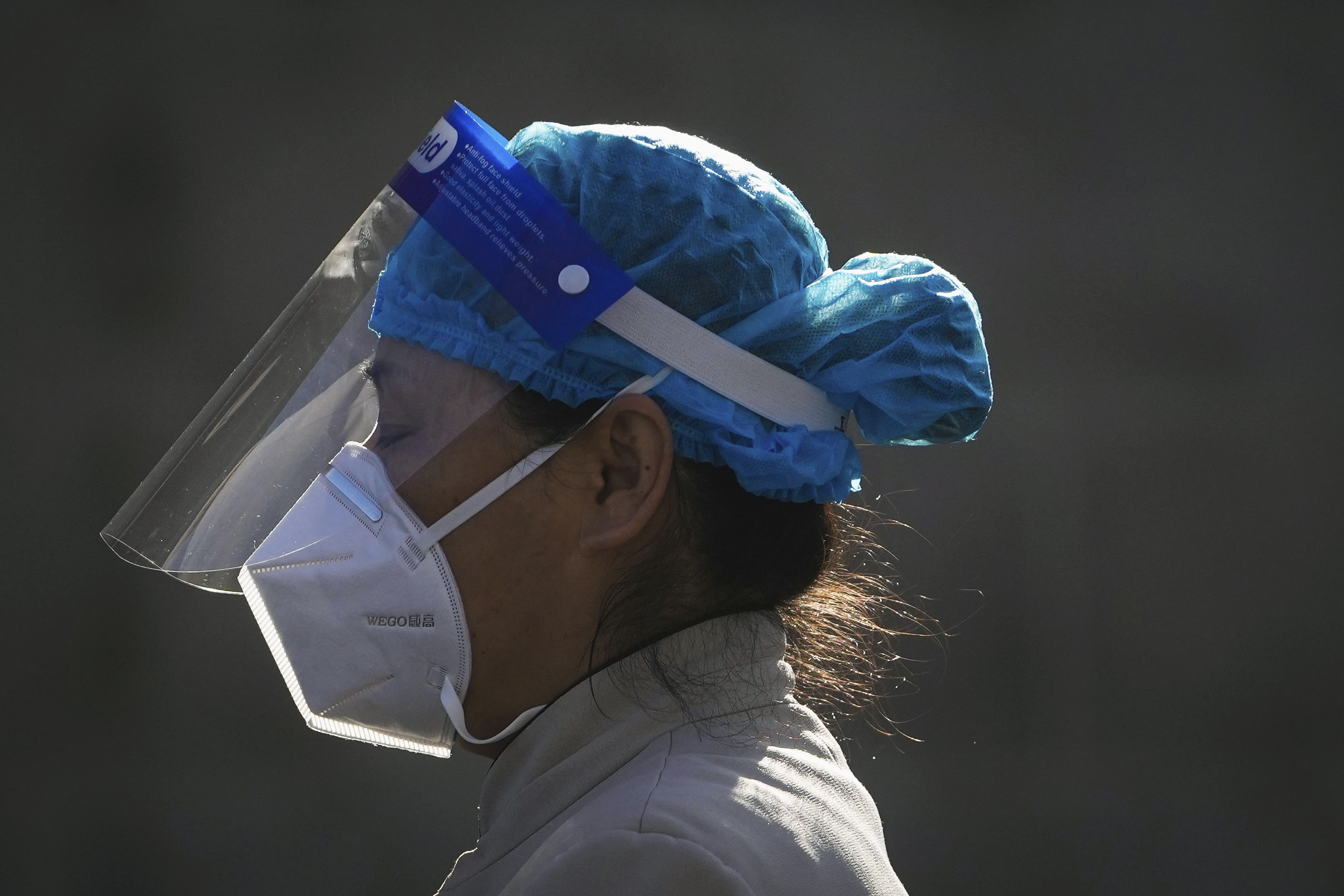 A close up of a woman in personal protective equipment including head covering, N95 mask and face shield