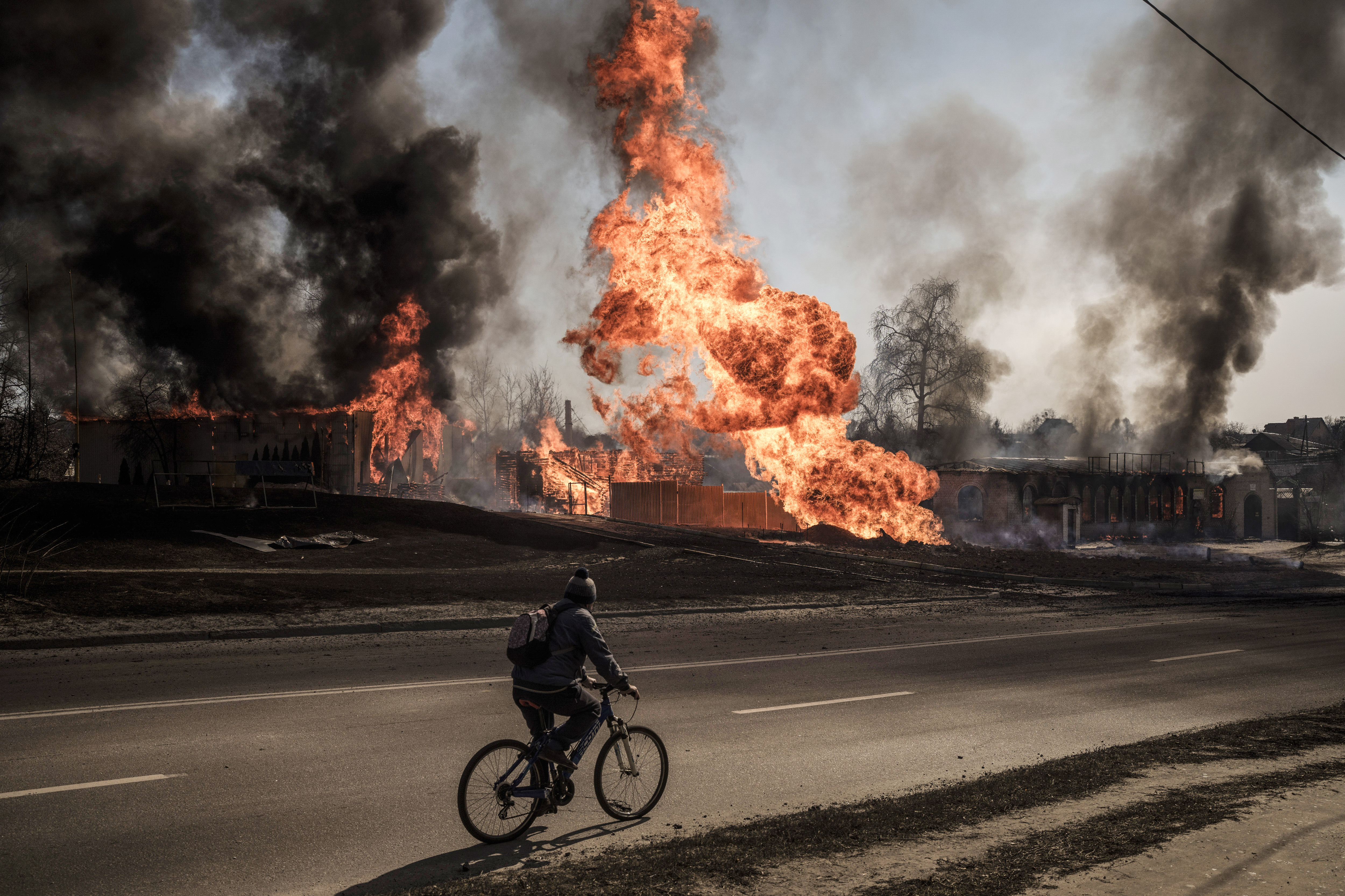 A man rides his bicycle past flames and smoke rising from a fire following a Russian attack in Kharkiv