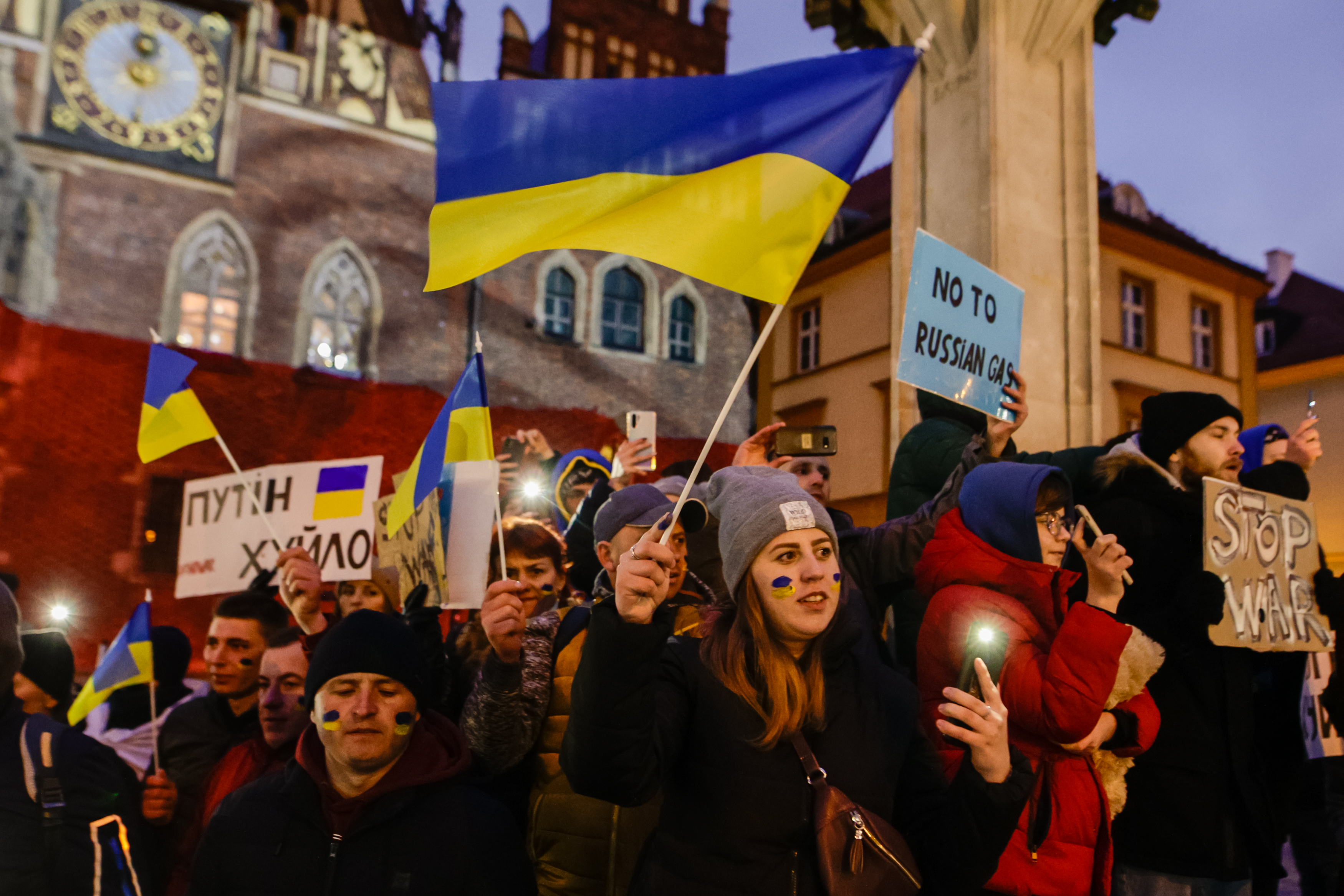 A group of people at an anti-war protest holding signs and Ukrainian flags.