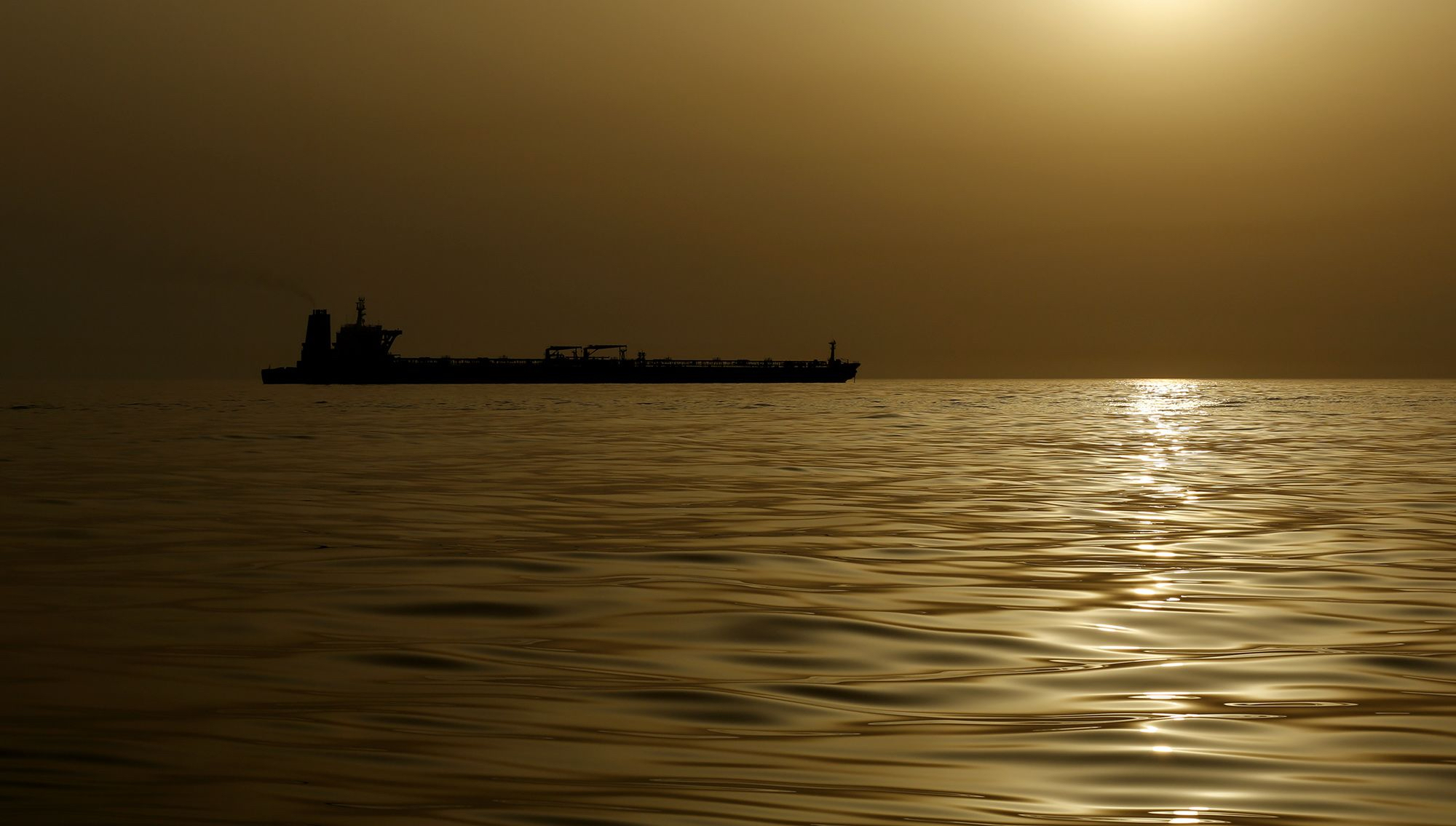 An oil tanker is silhouetted against the hazy sky