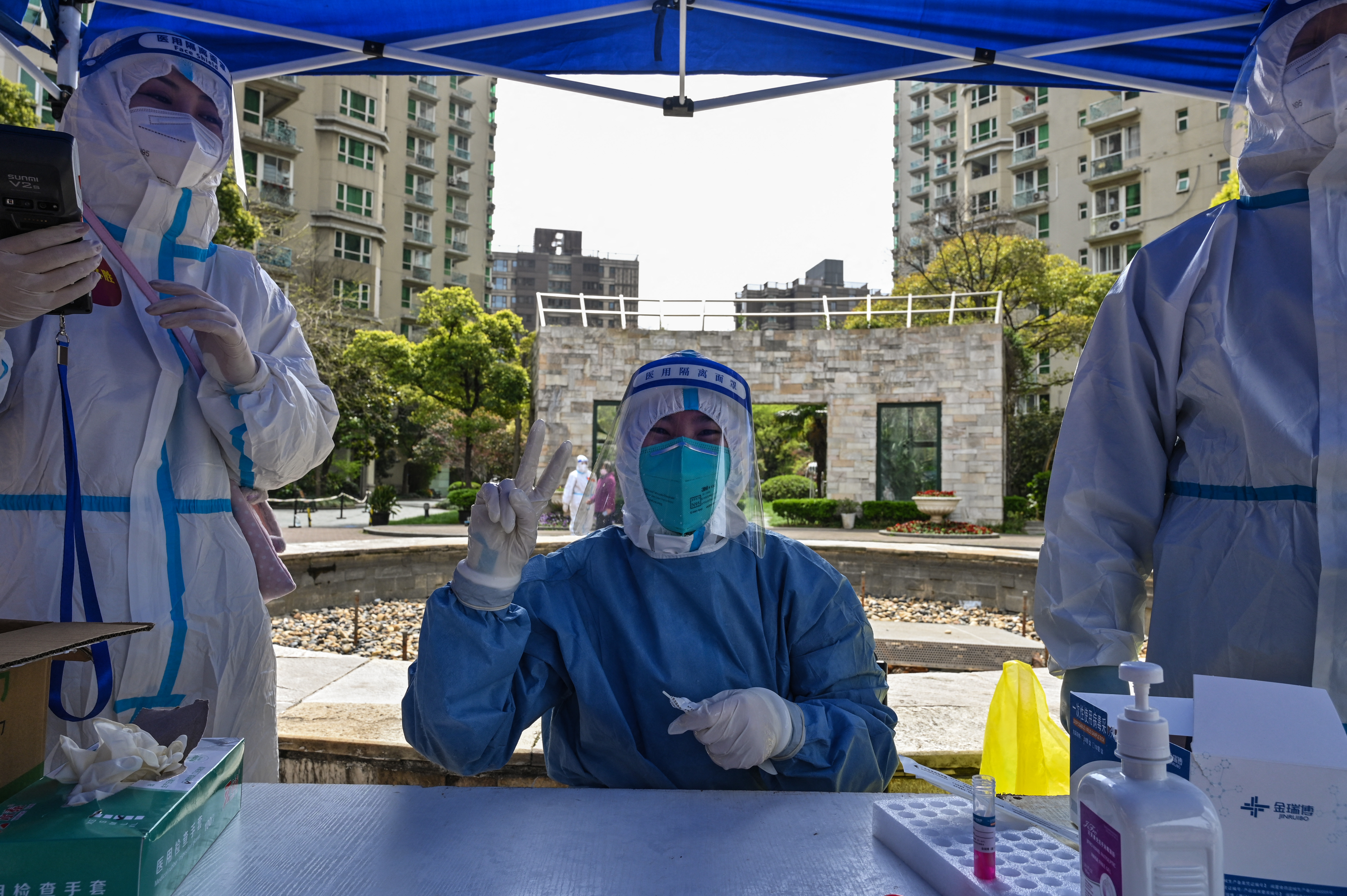 A health worker in full PPE including blue gown, surgical gloves, mask, hat and face shield hokds up their hand at a temporary testing tent for COVid-19 at an apartment block in Jing'An, Shangai, China.