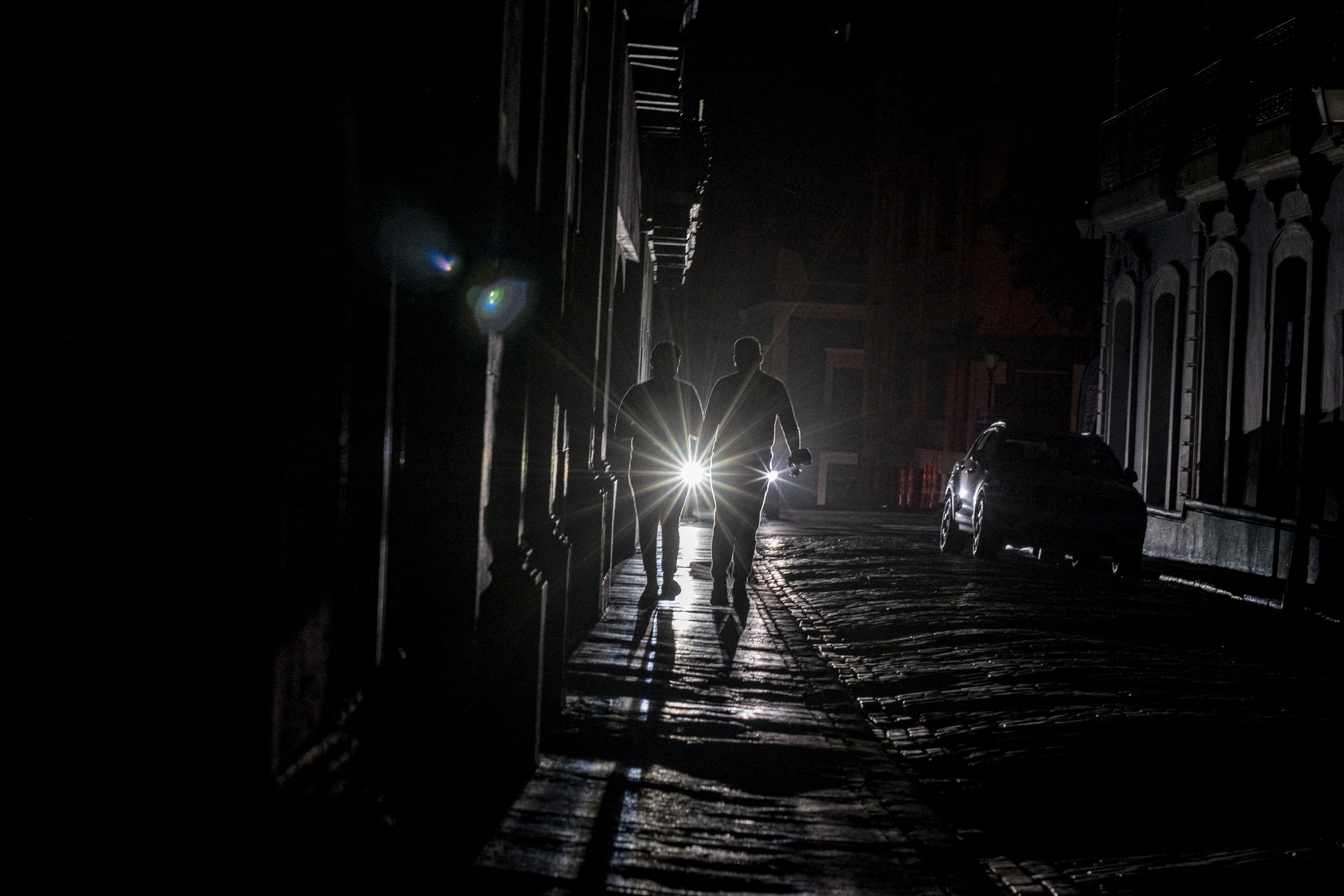 A cars headlights are seen past people walking on a dark in San Juan, Puerto Rico 