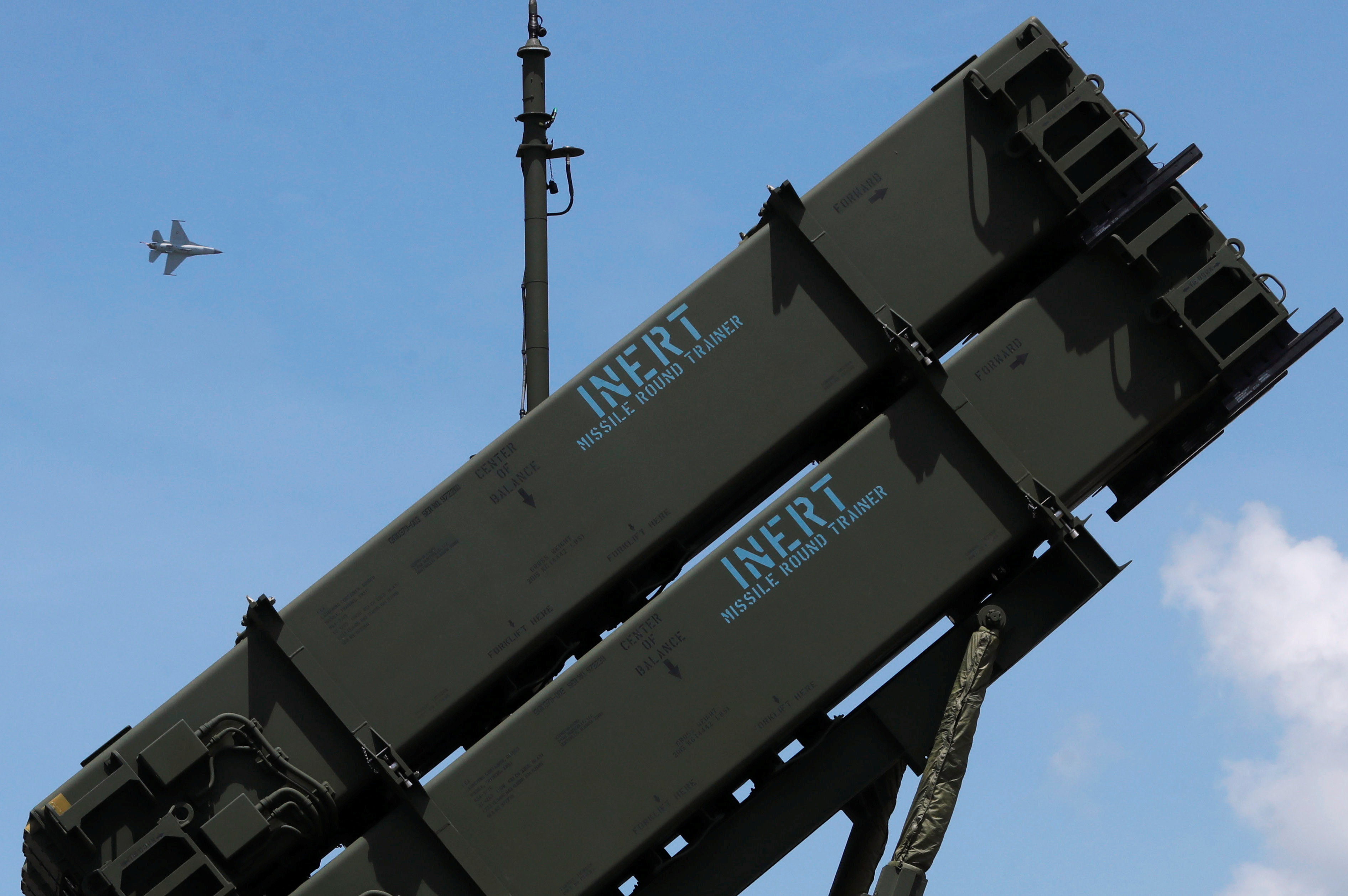 A patriot missile system against a bright blue sky with a Taiwan airforce F16 in the background.