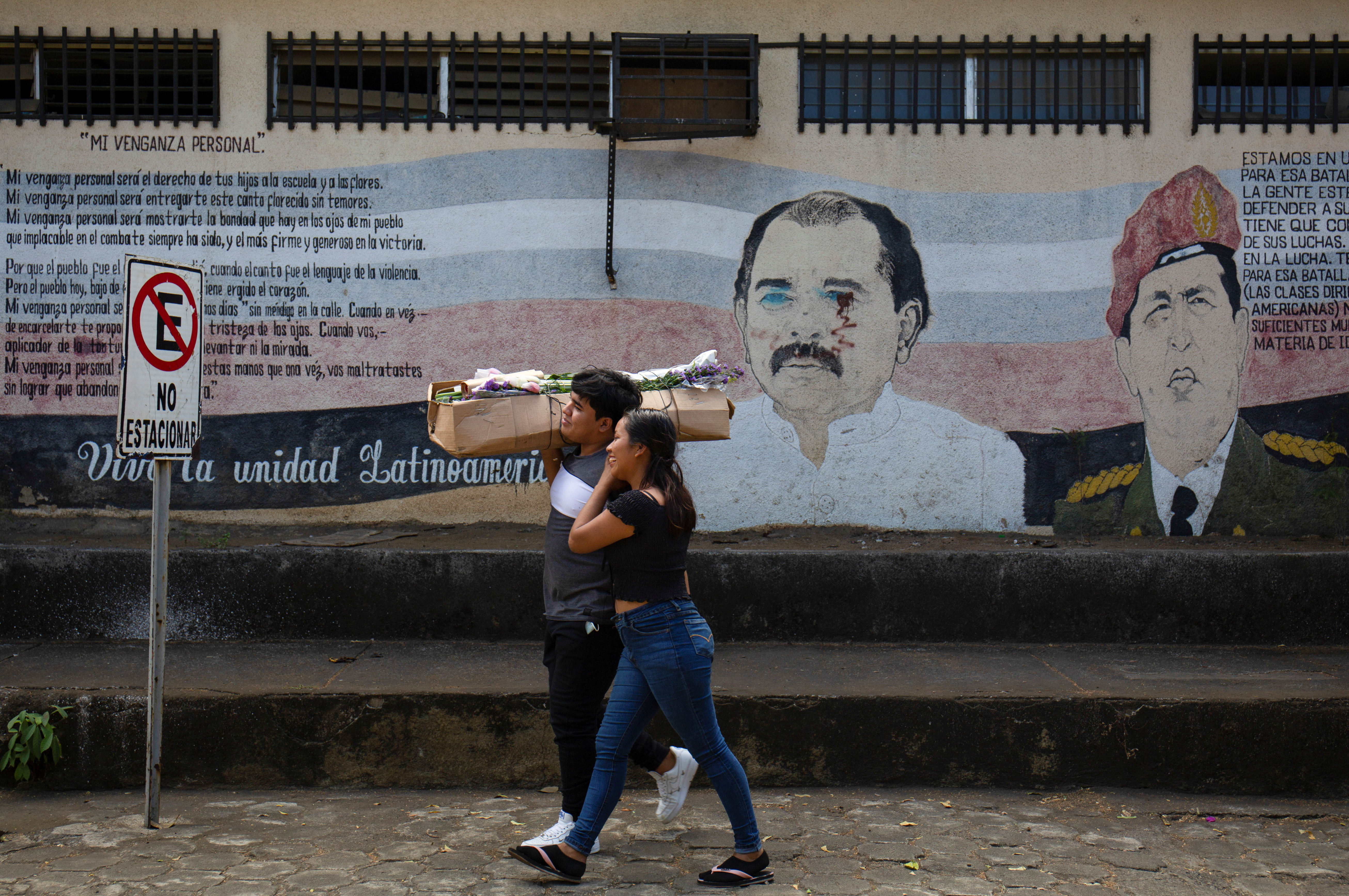 People walk by a mural showing Daniel Ortega and Hugo Chavez