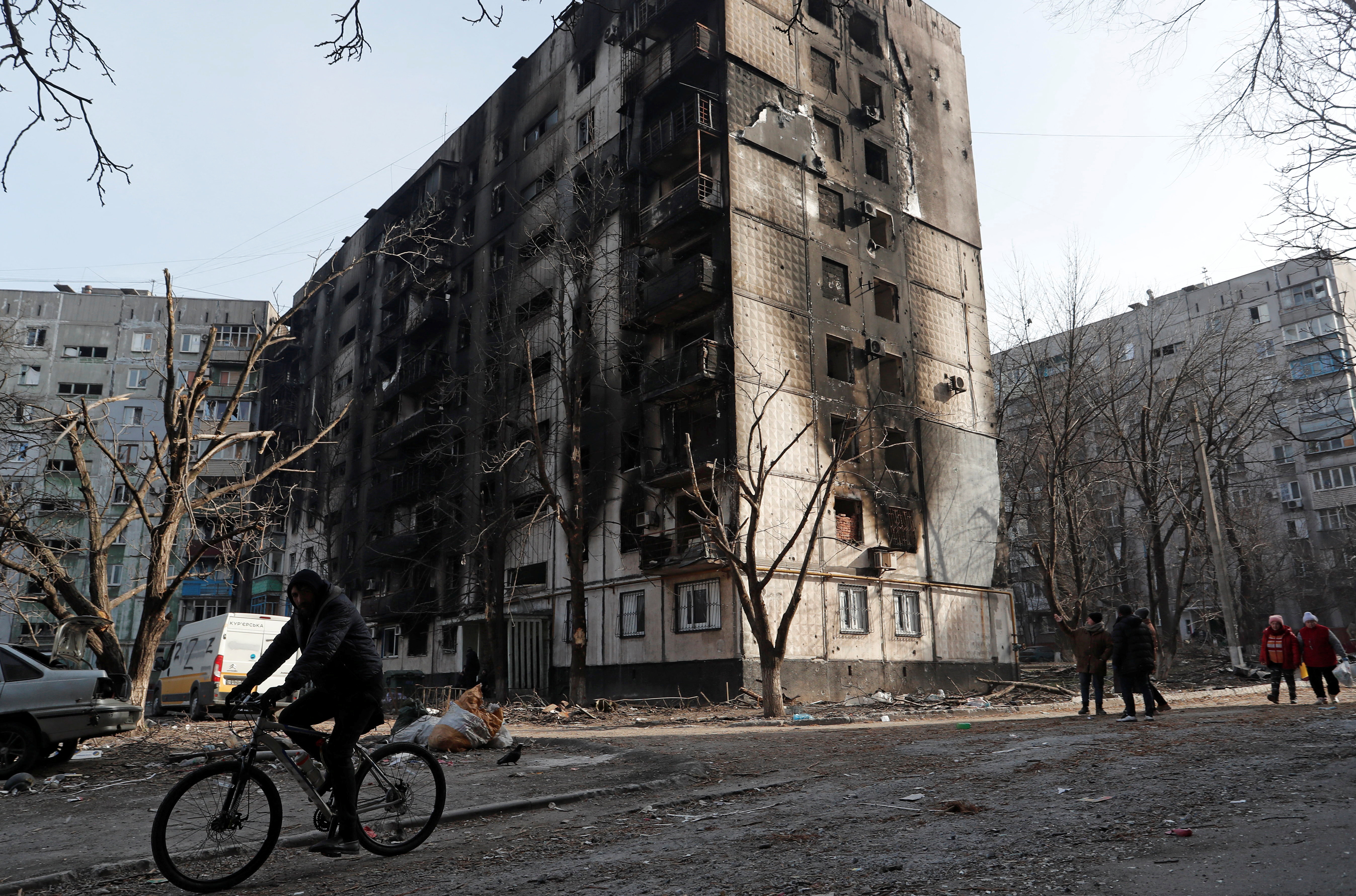 A local resident rides a bicycle past a damaged apartment building