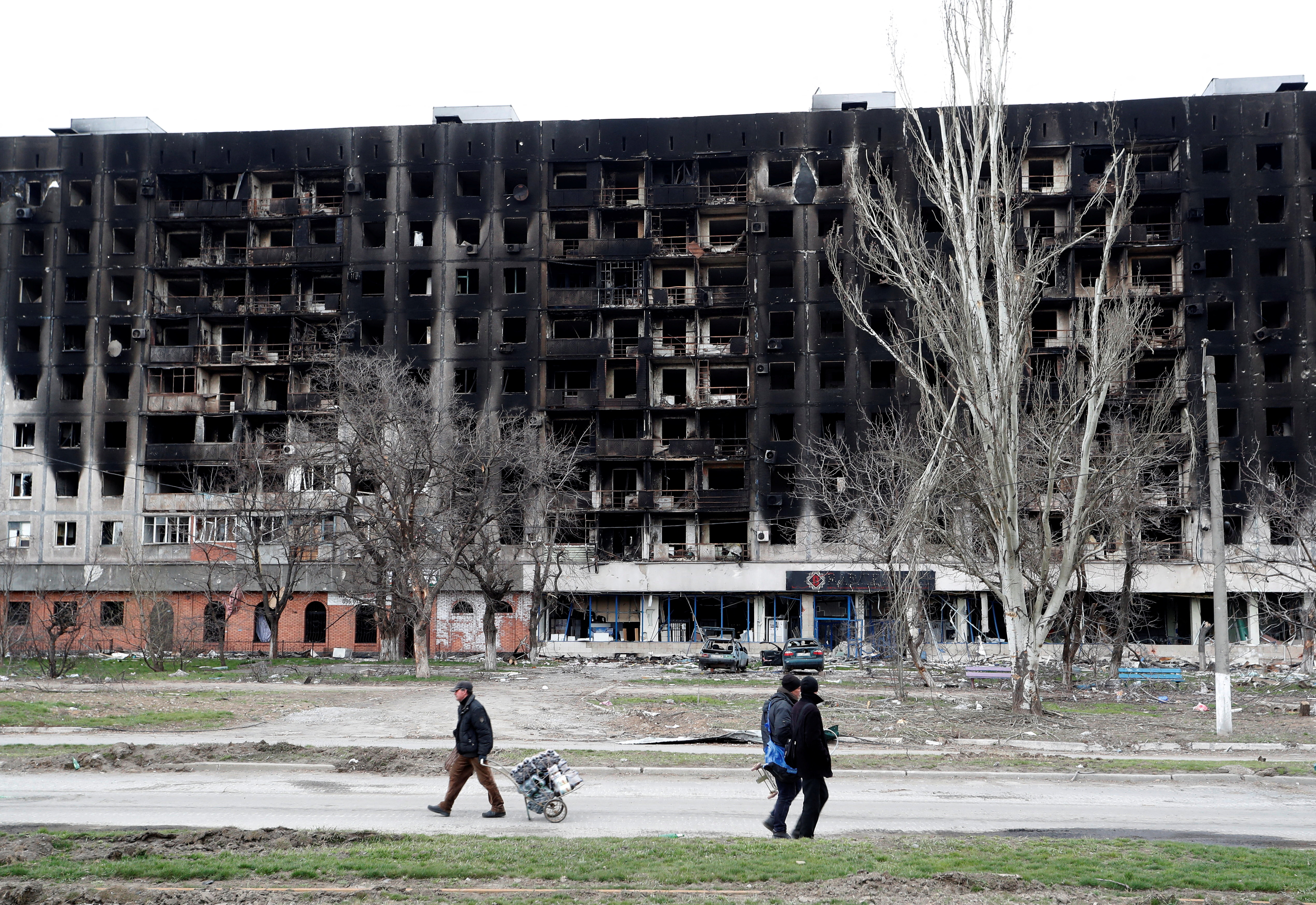 Local residents walk past a burned building during Ukraine-Russia conflict in the southern port city of Mariupol
