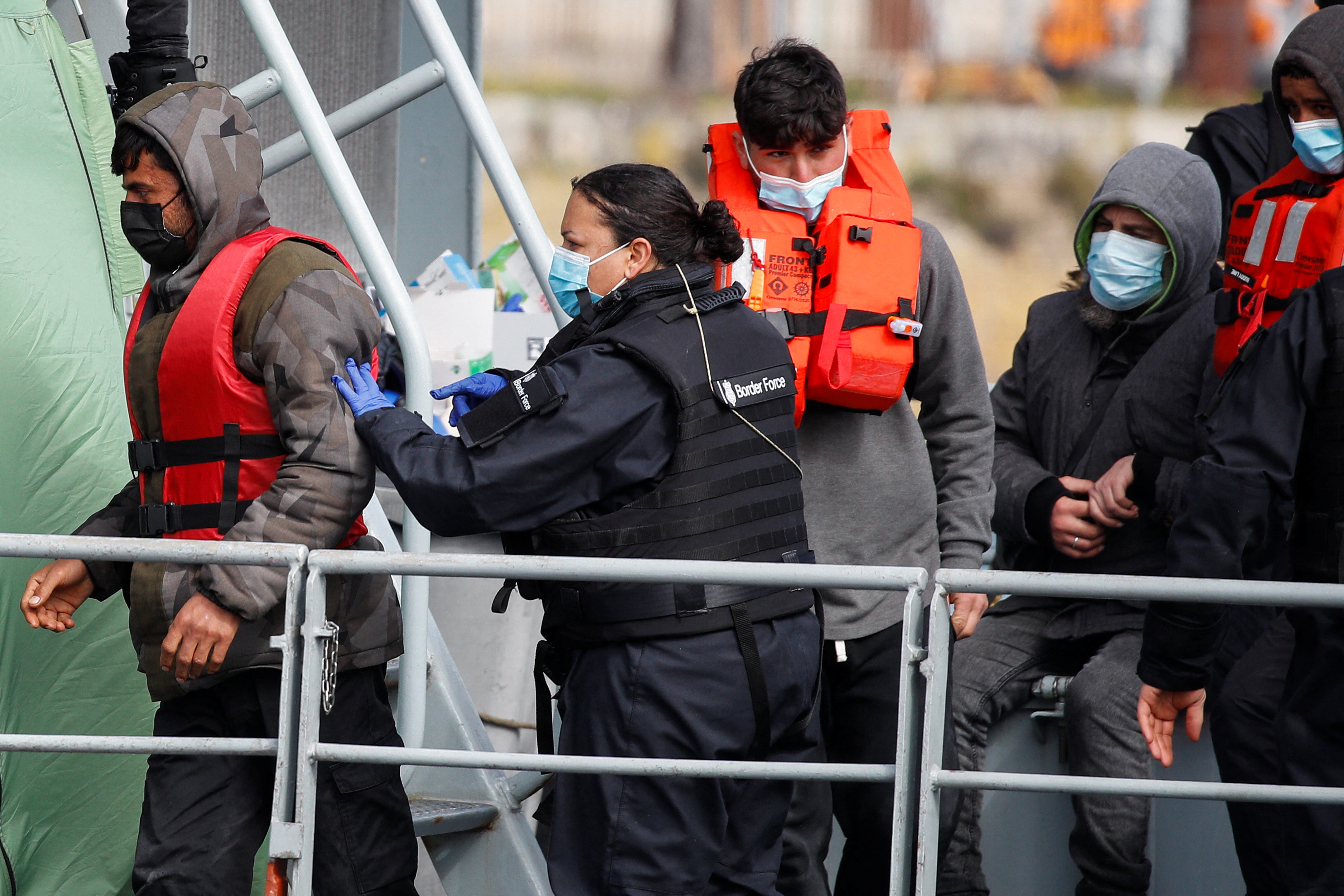 A member of Britain's border force is seen escorting migrants and refugees