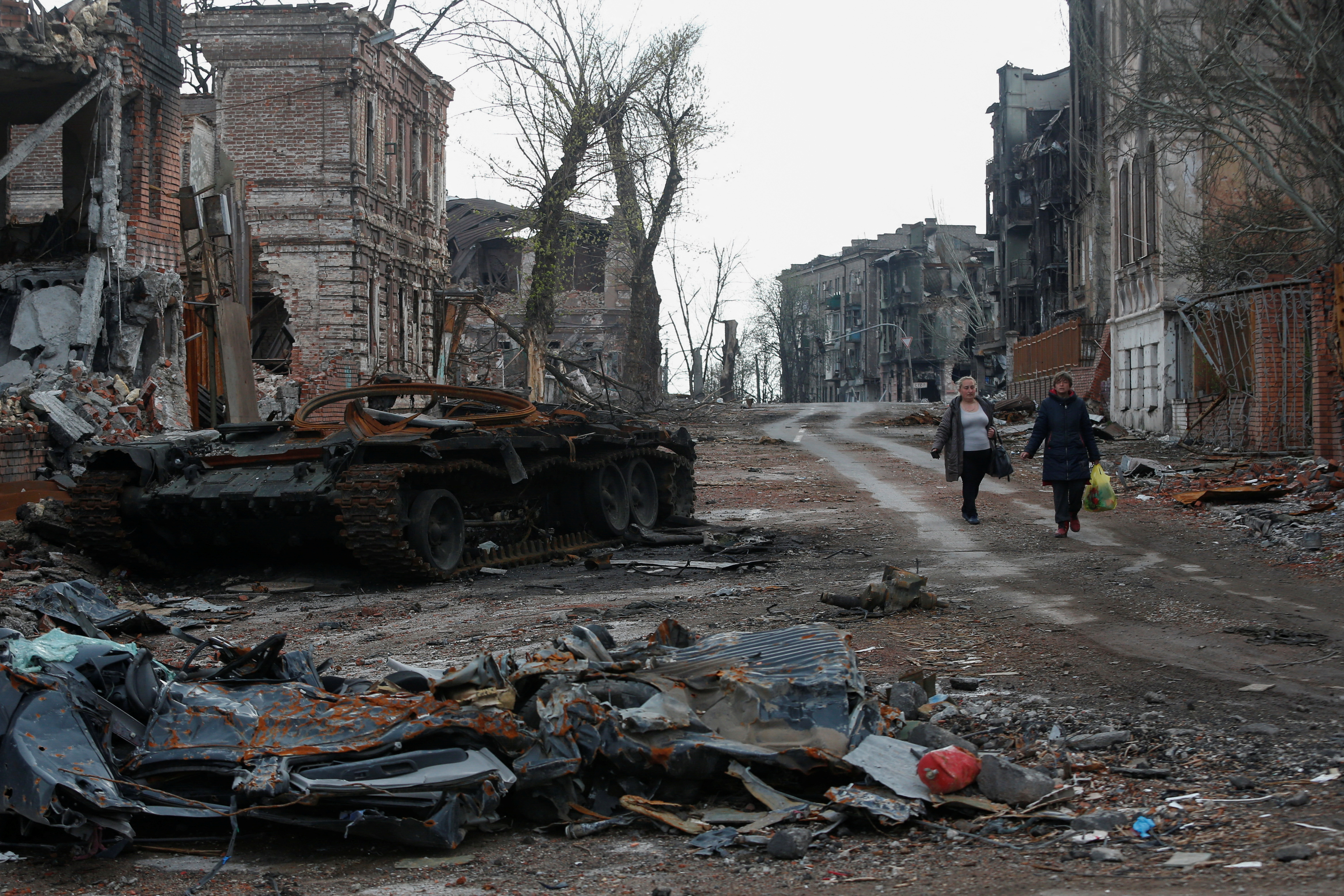 People walk down a street where the buildings have been left in ruins by bombing.