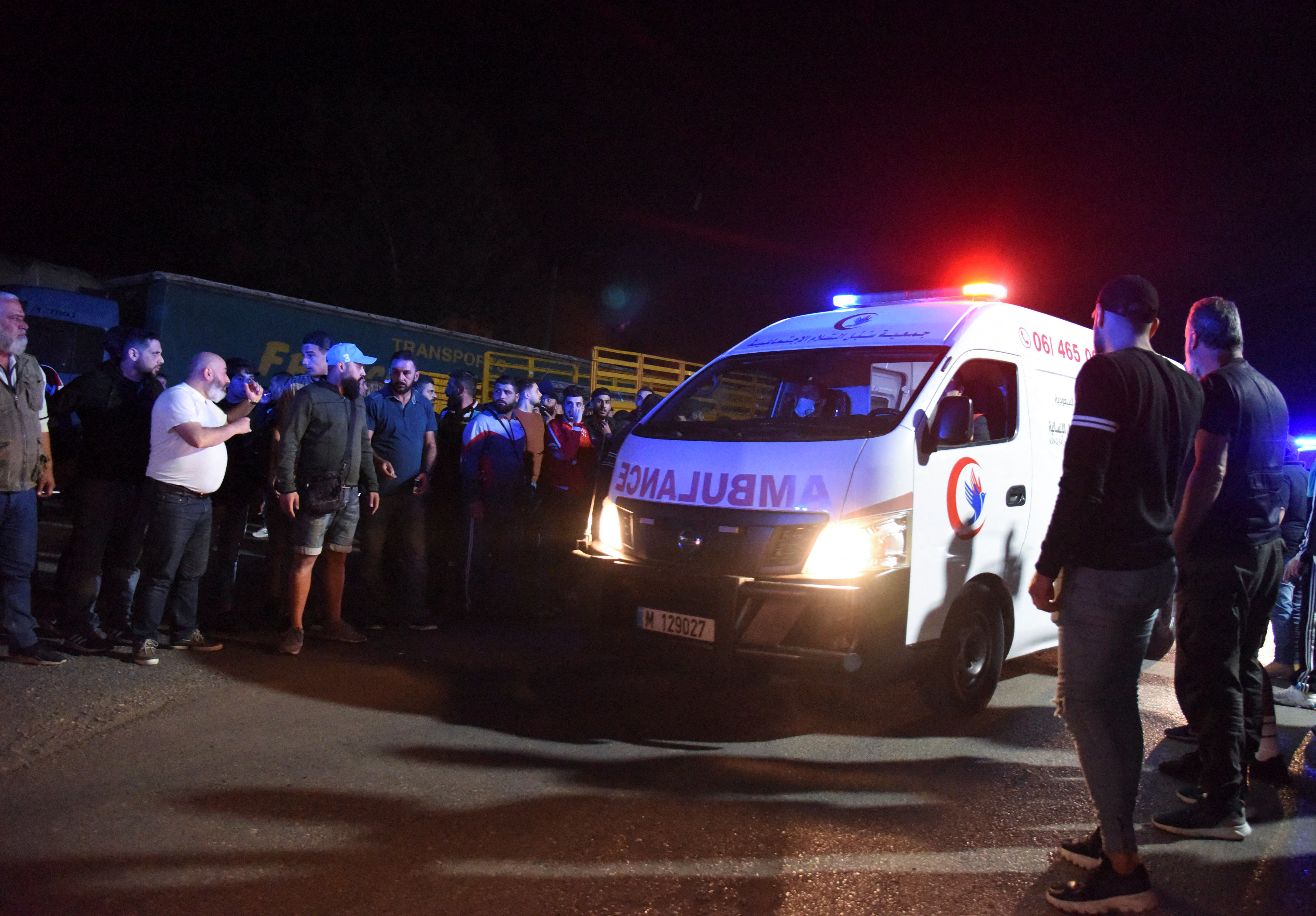 People gather as an ambulance drives following the sinking of a boat off the coast of Lebanon's northern port city of Tripoli
