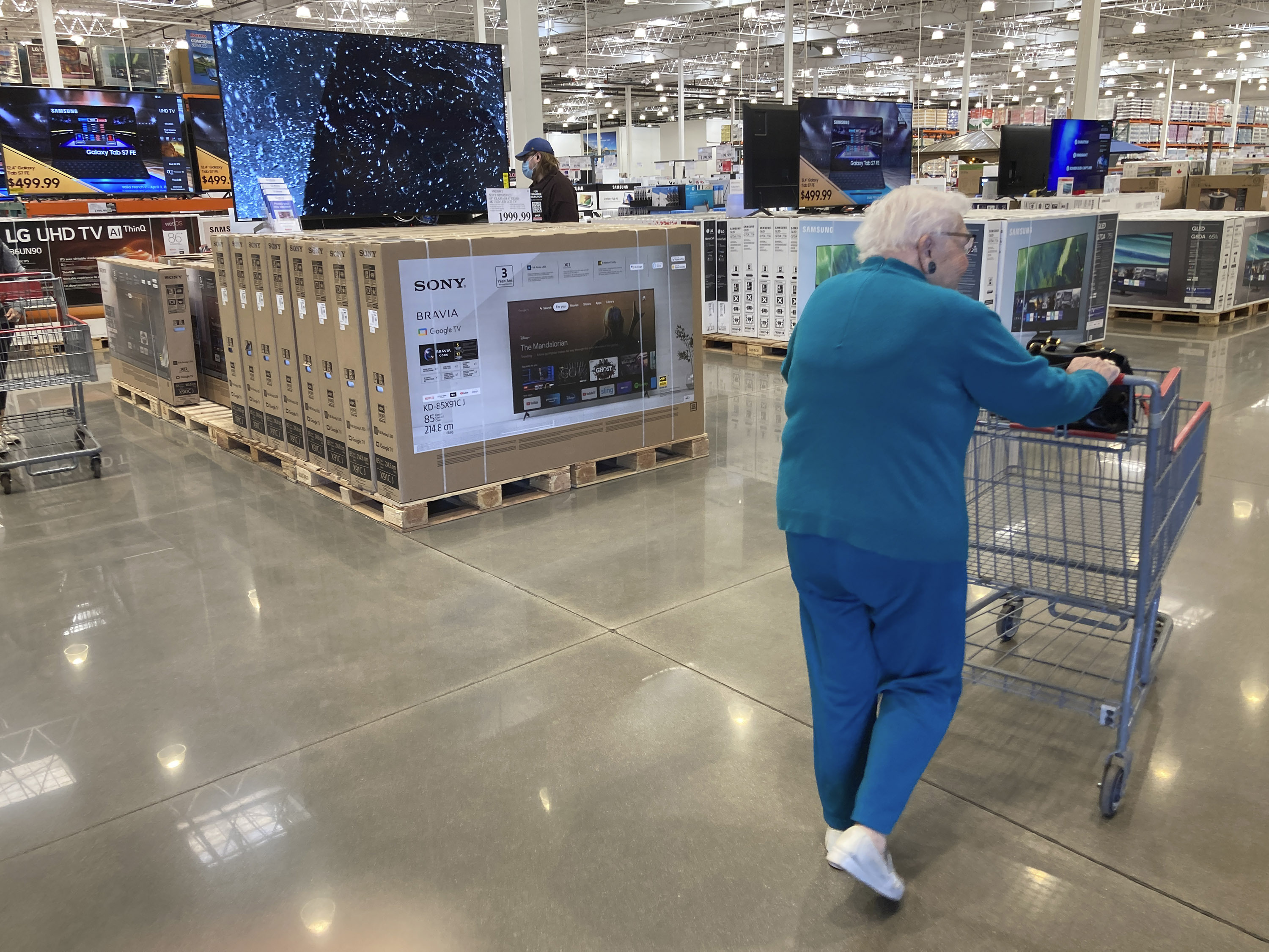 A shopper guides a cart past a display of big-screen television sets in a Costco warehouse